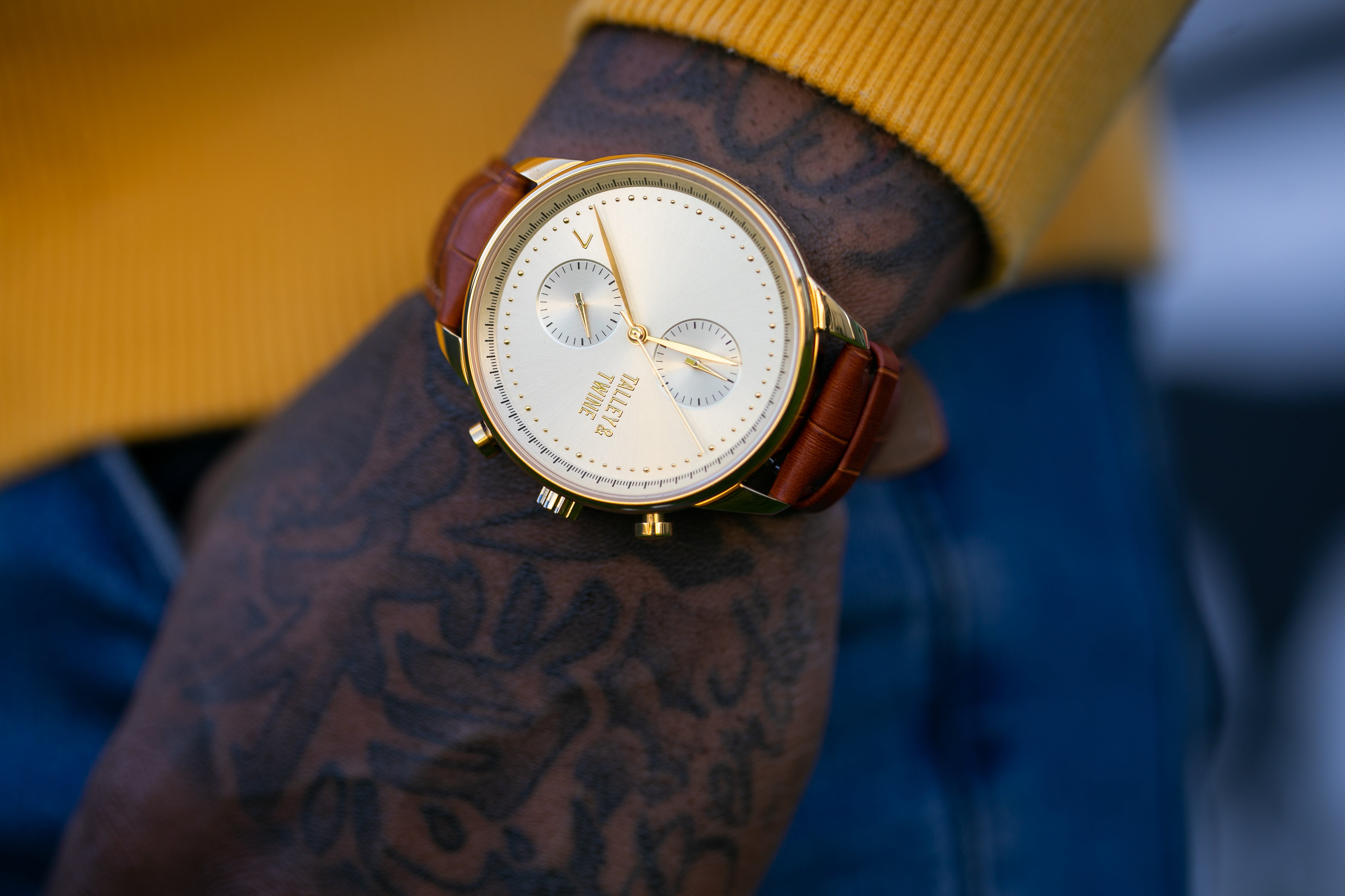 A Tally & Twine watch with a leather strap worn by a model against their jeans and a bright yellow sweater. 