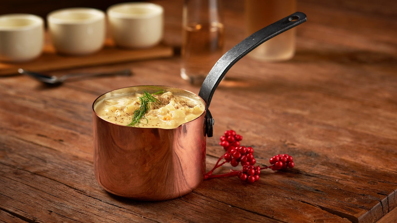 A bowl of lobster chowder against a wooden kitchen counter.