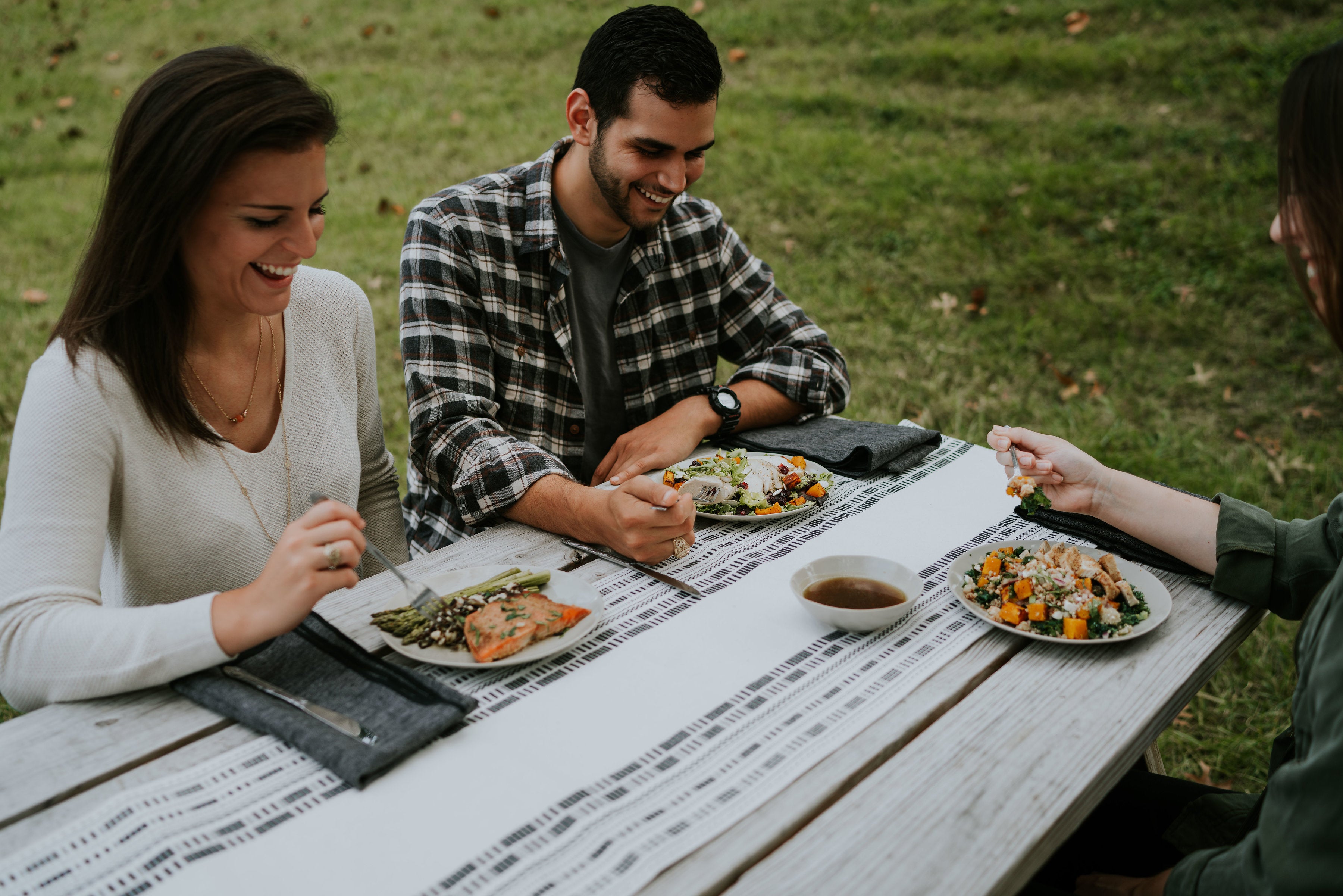 A group of three customers eating Eat Well Nashville meals on a picnic table. 