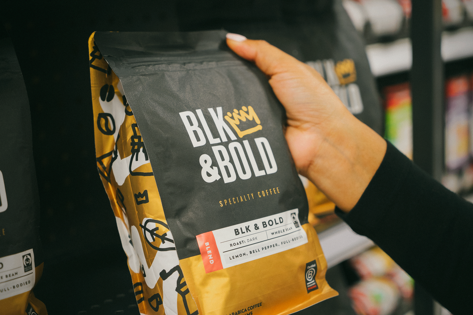 A package of BLK & Bold coffee held by a hand against some retail shelves. 