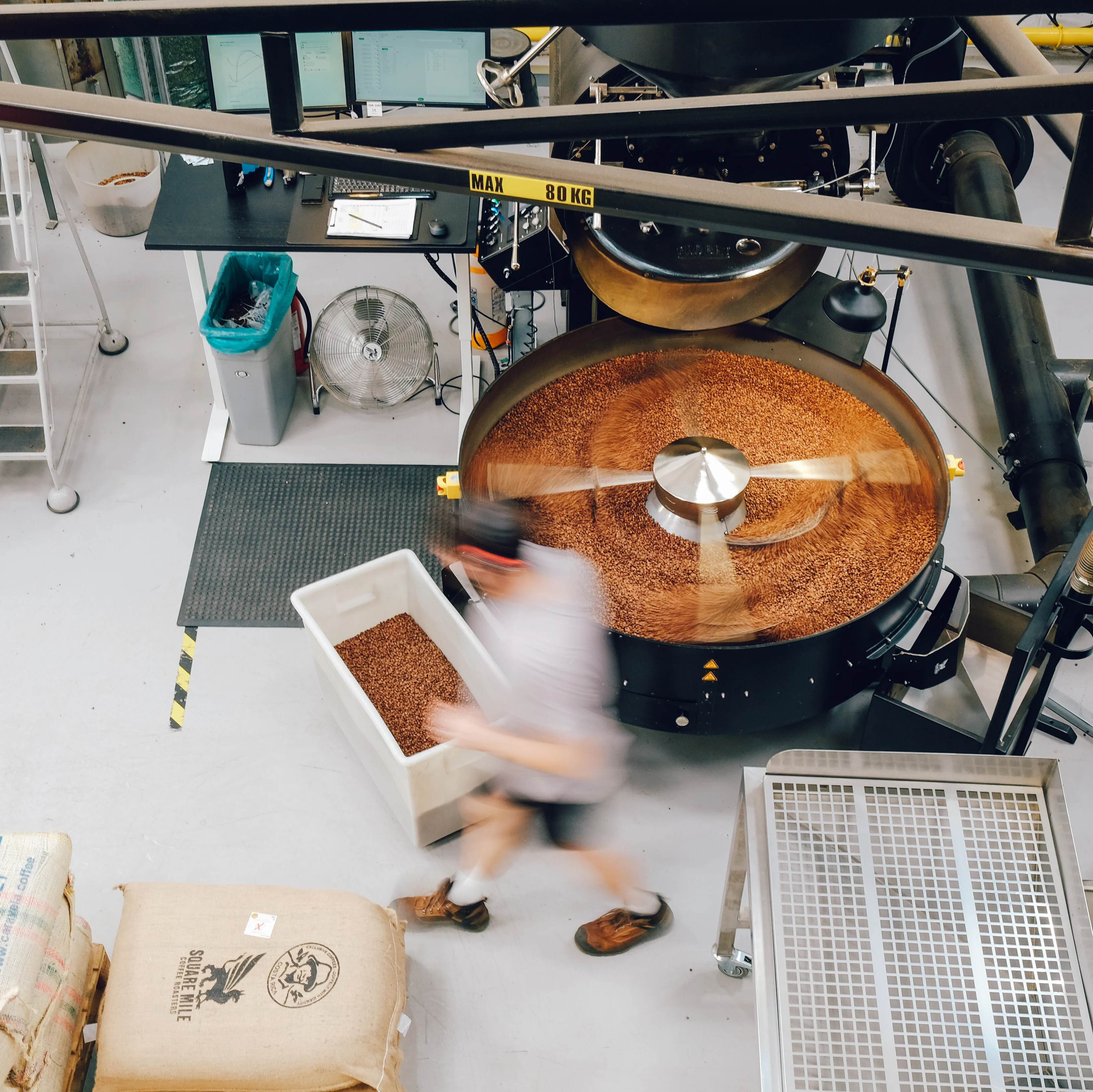 A worker walking beside a machine roasting coffee beans inside Square Mile Coffee Roasters. 