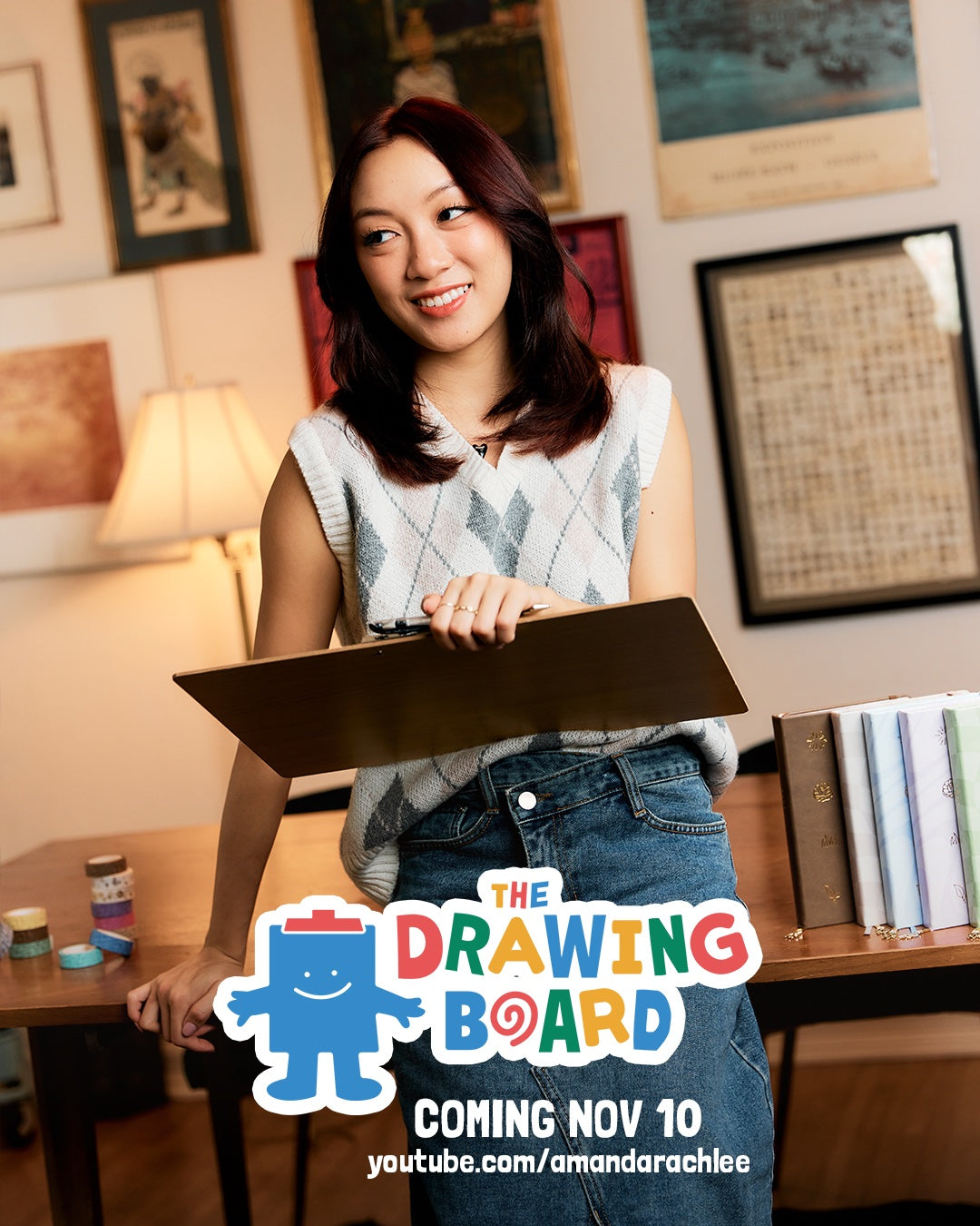 Amanda Rach Lee in a sweater vest and jeans holding a drawing board. 