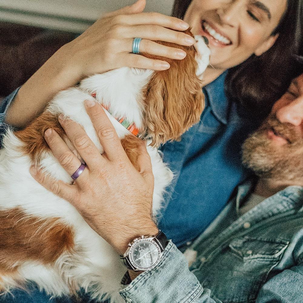 Two people wearing silicone engagement rings pet a dog
