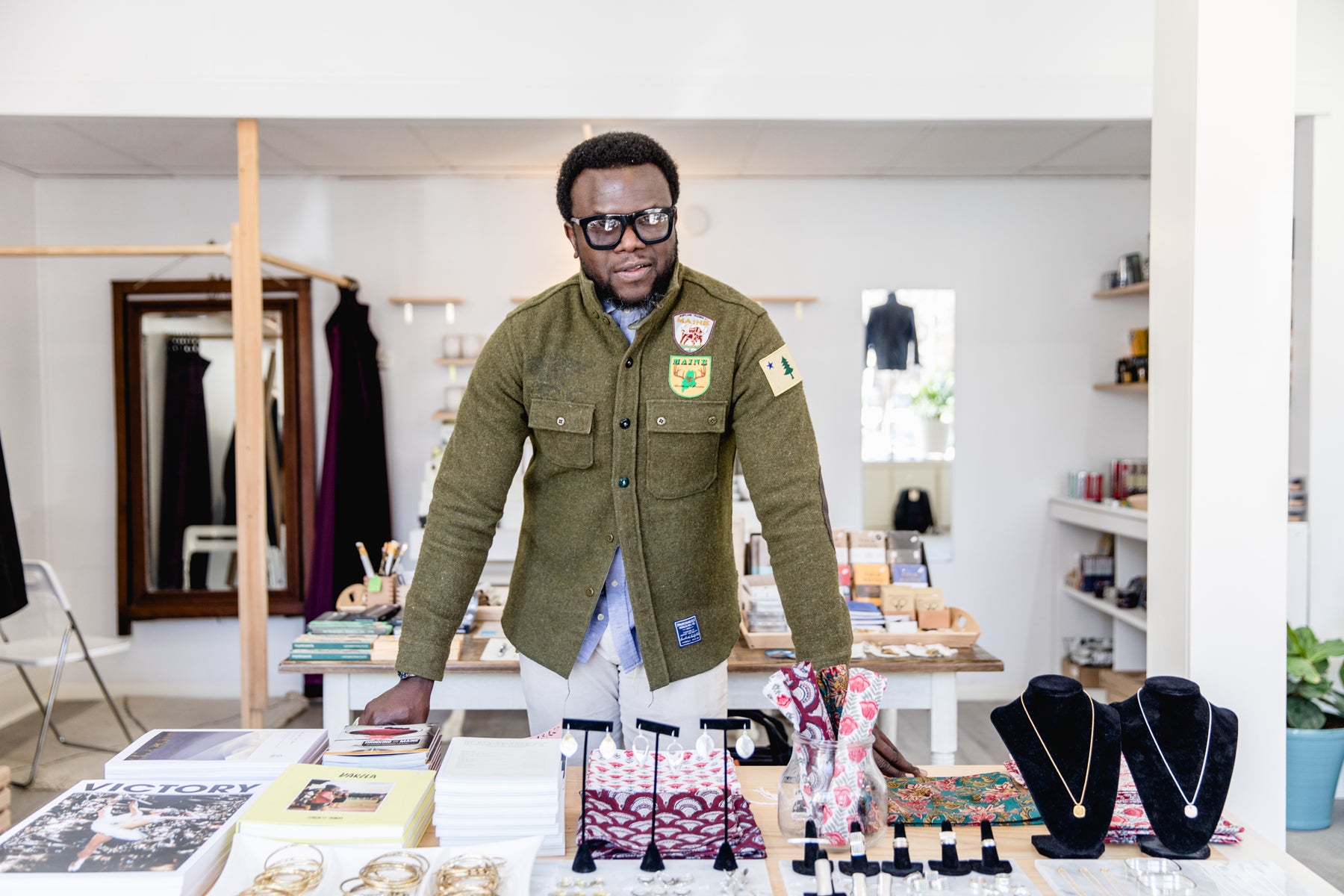 Portland Trading Co. founder Kazeem Lawal leans on a display table covered in books, jewelry, and lifestyle products. 
