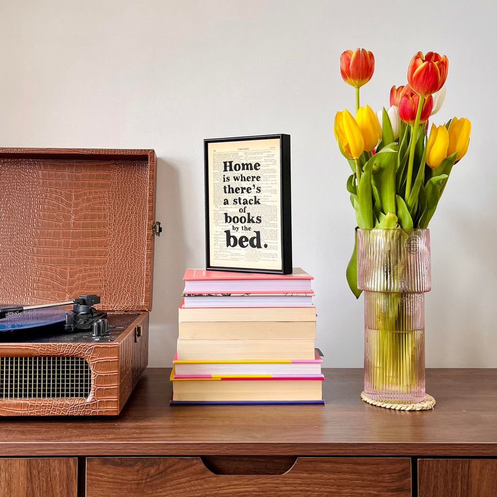 Bookishly print on top of a stack of books and next to a record player and flowers
