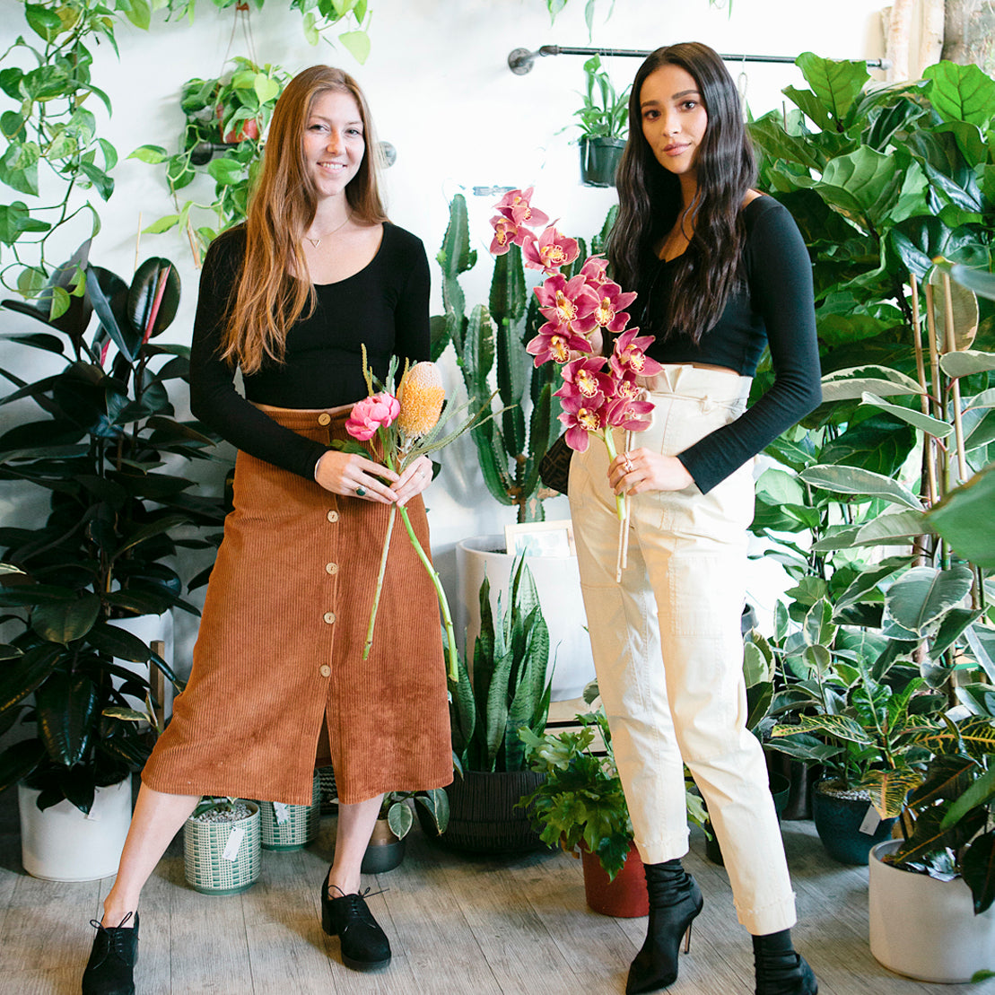 Alexandra Scholtz (left), owner of WildFlora, and Shay Mitchell (right), pose with flowers in front of a plant-filled wall.