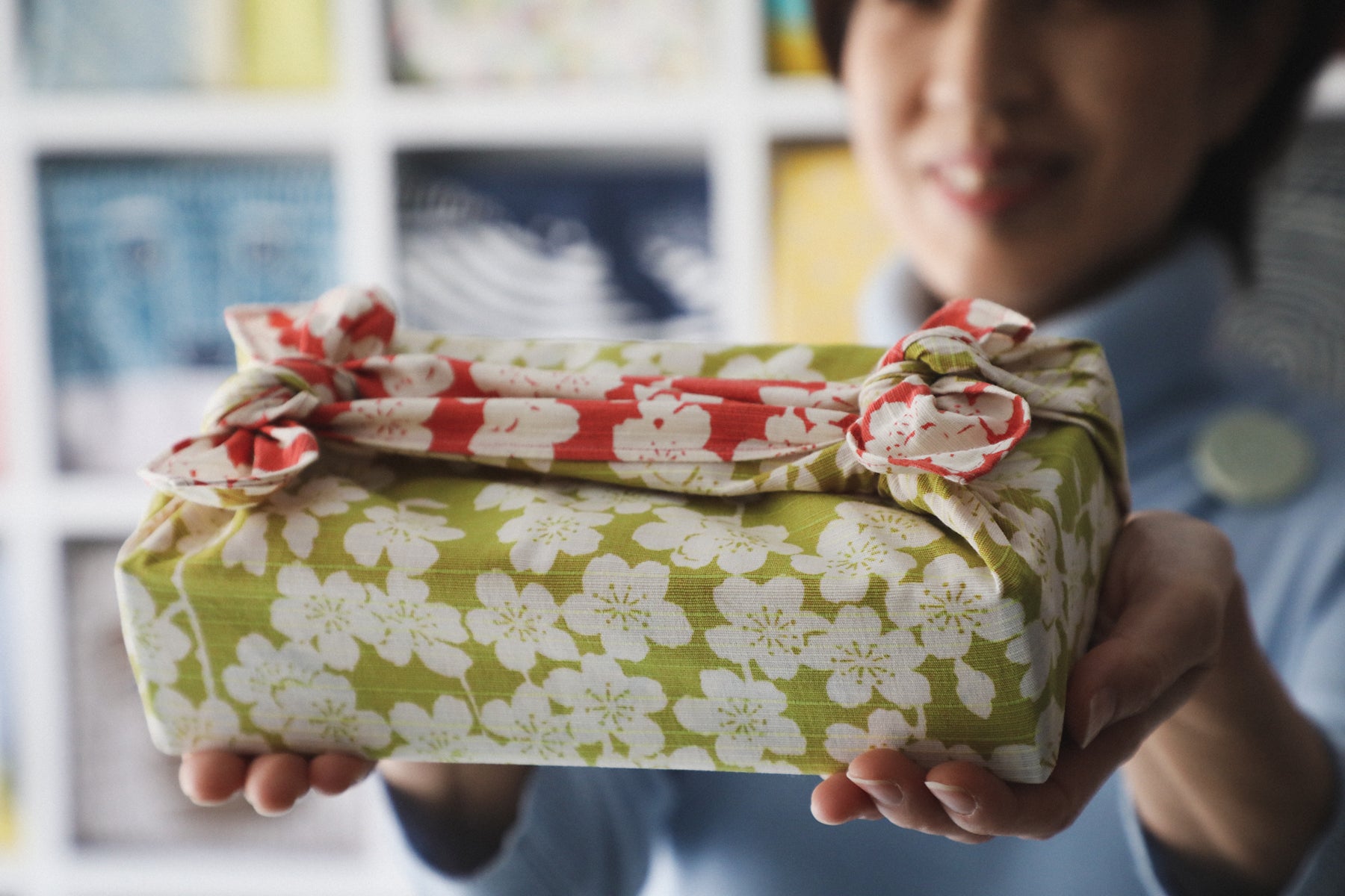 A gift is covered with furoshiki (wrapping cloth) that is green and red with white sakura (cherry blossom) flowers. 