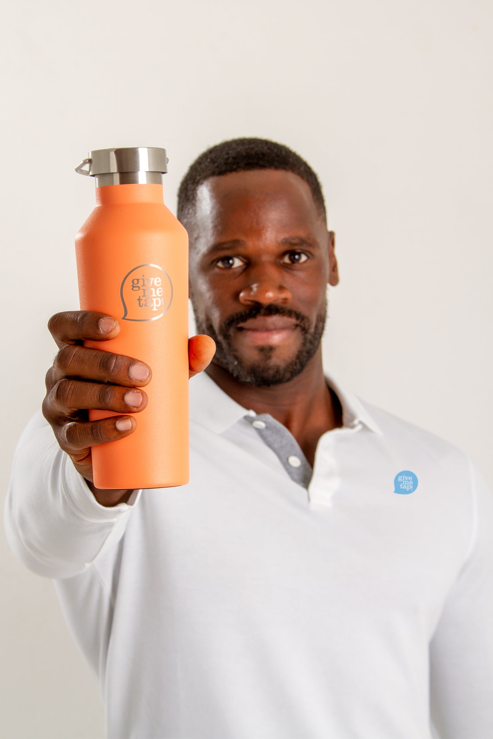 Edwin Broni-Mensah in a white shirt with the GiveMeTap logo holding up an orange GiveMeTap water bottle. 