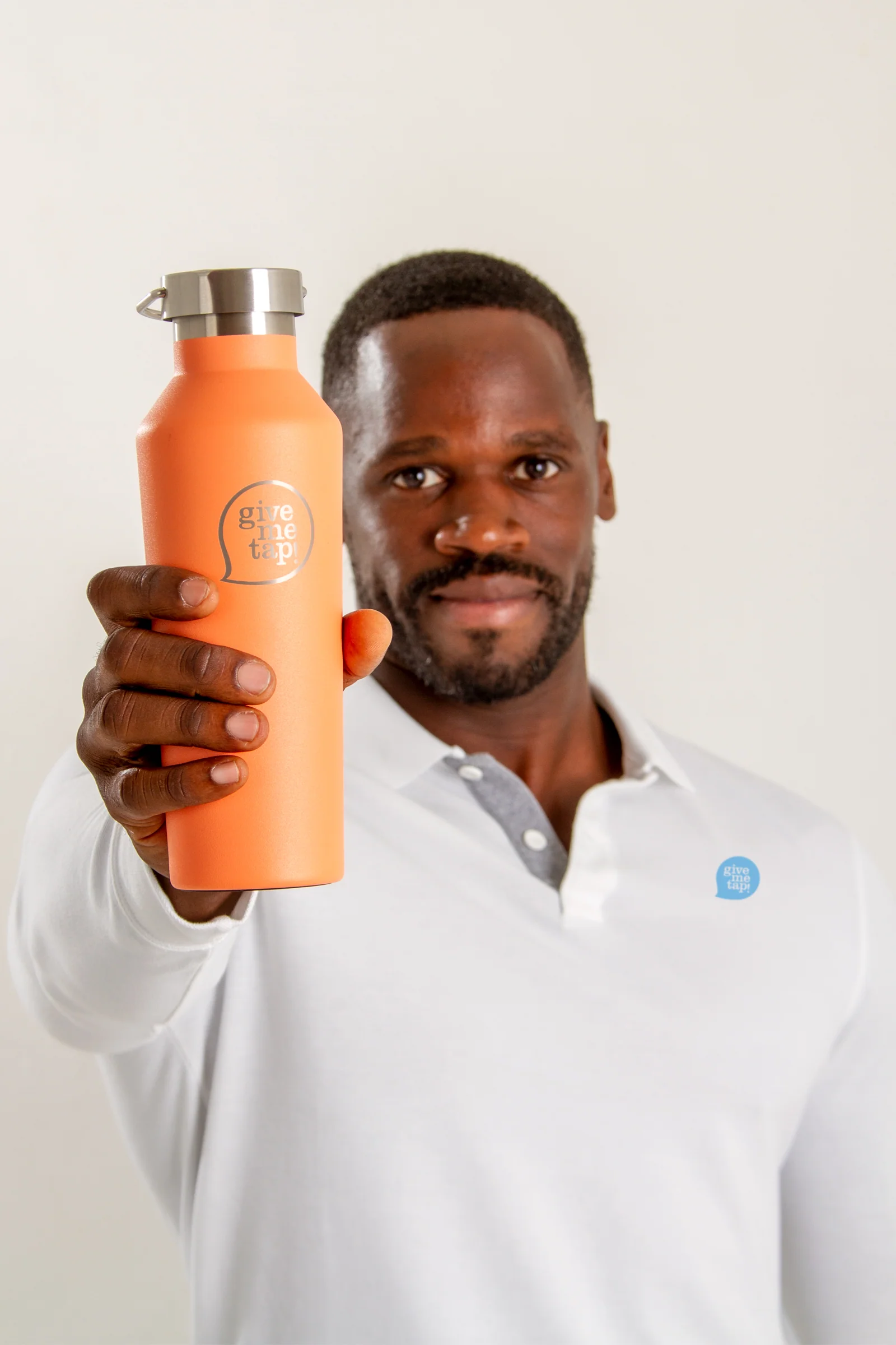 Edwin Broni-Mensah in a white shirt with the GiveMeTap logo holding up an orange GiveMeTap water bottle. 