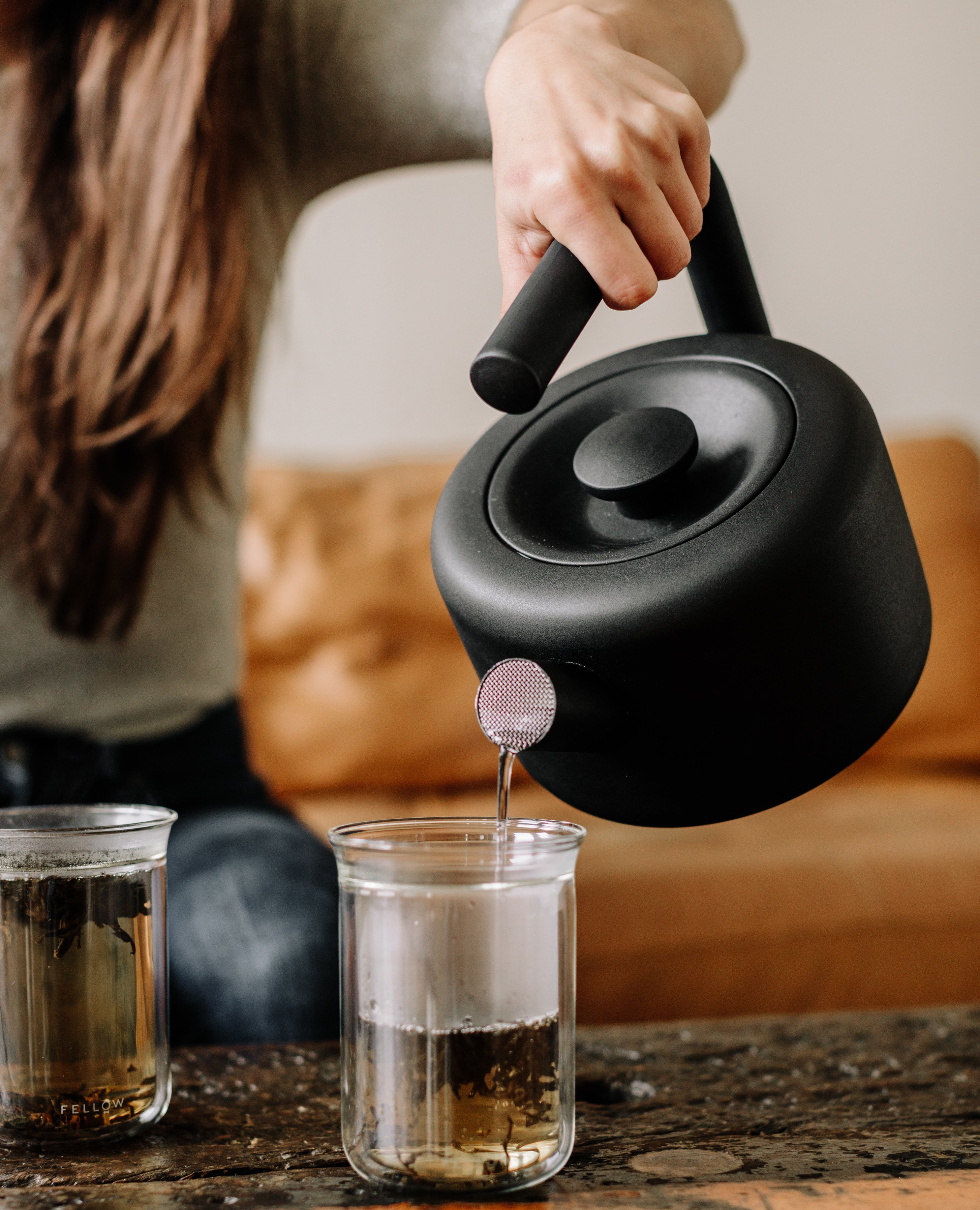 A model pours hot water out of the Clyde stovetop tea kettle into a Stagg Tasting Glass.