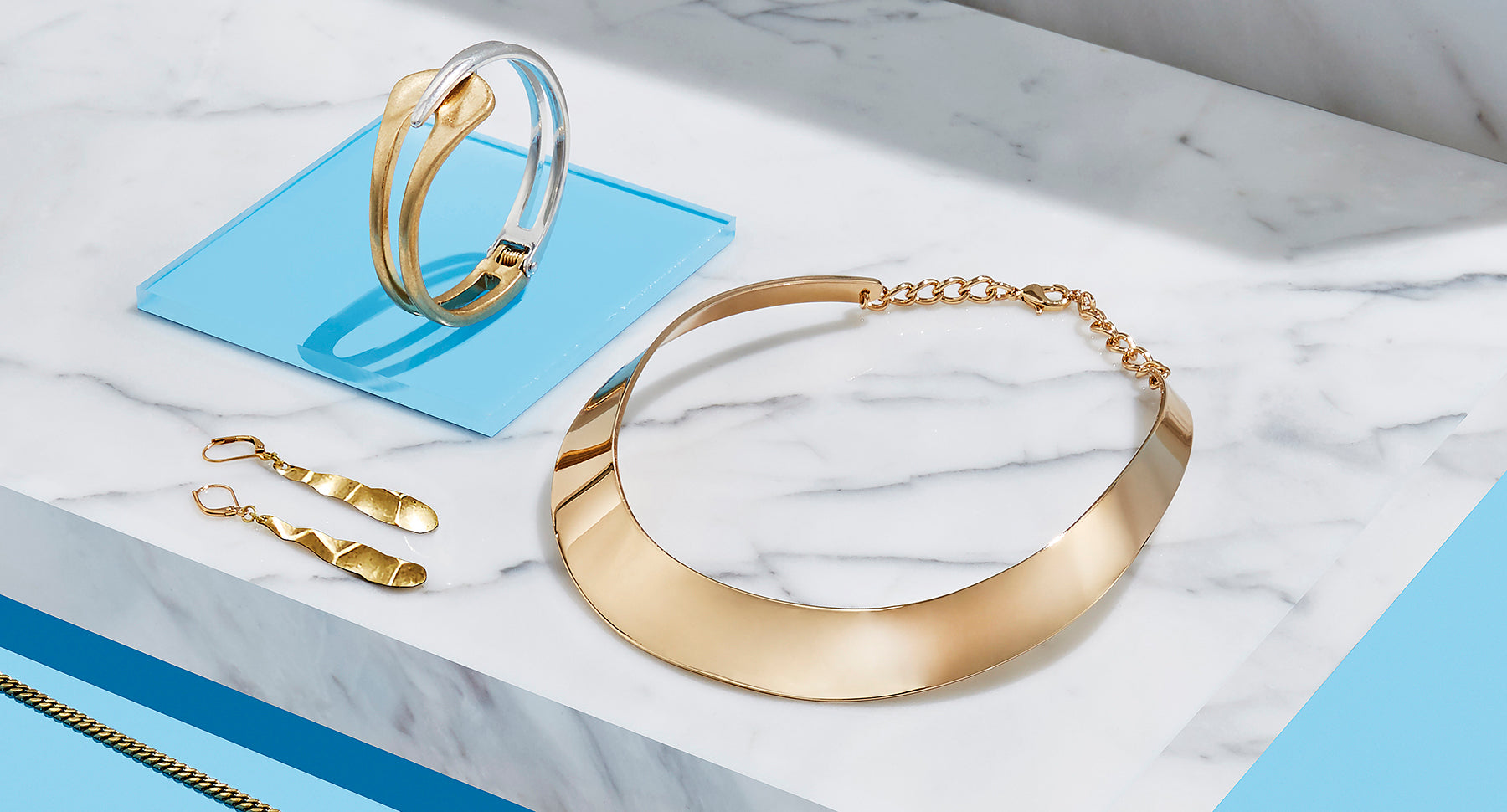 A gold bracelet, necklace, and earrings sitting on a white marble slab. 