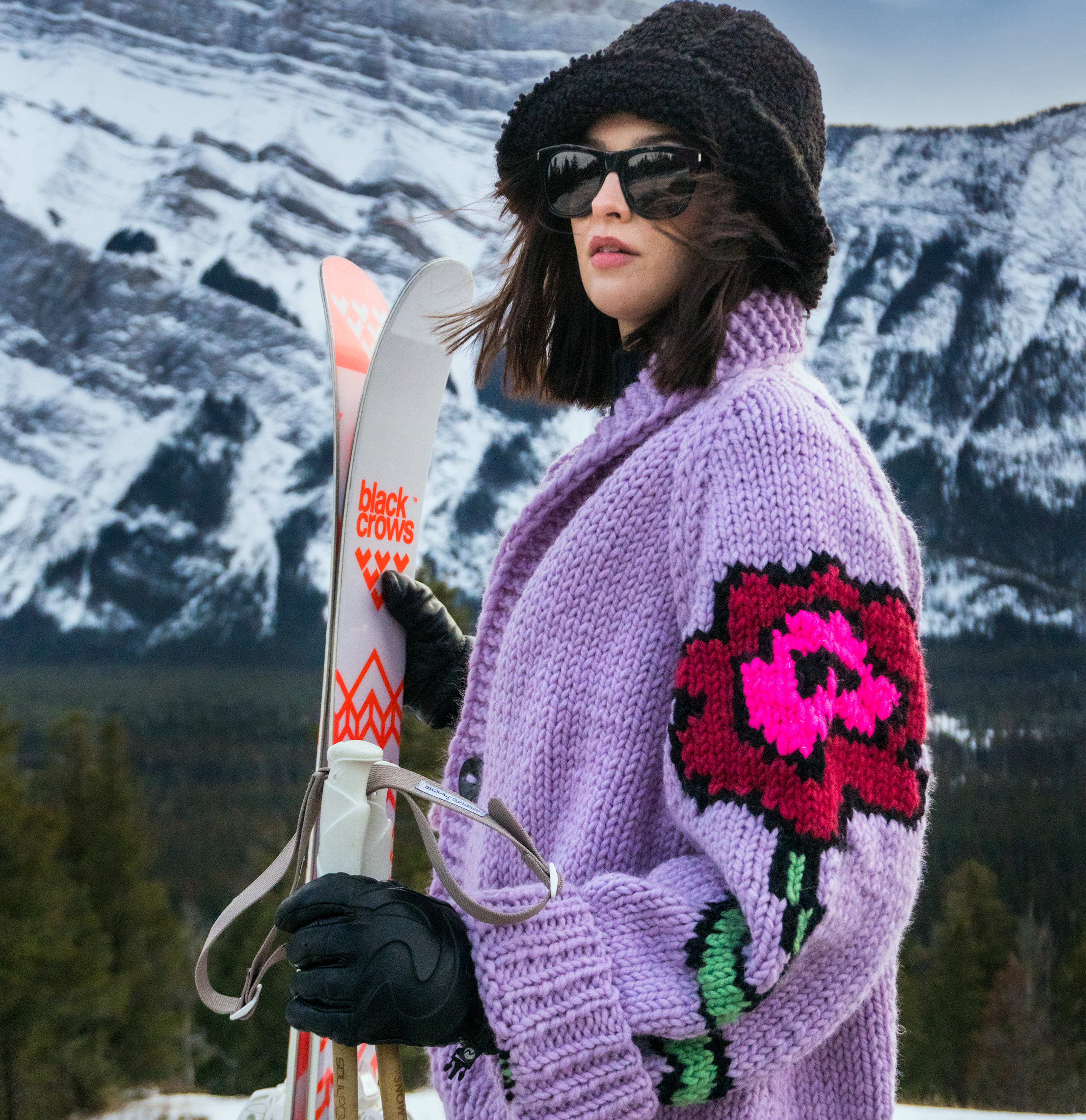 a model holds a pair of skis and poles while wearing the flower jacket in the color lilac.