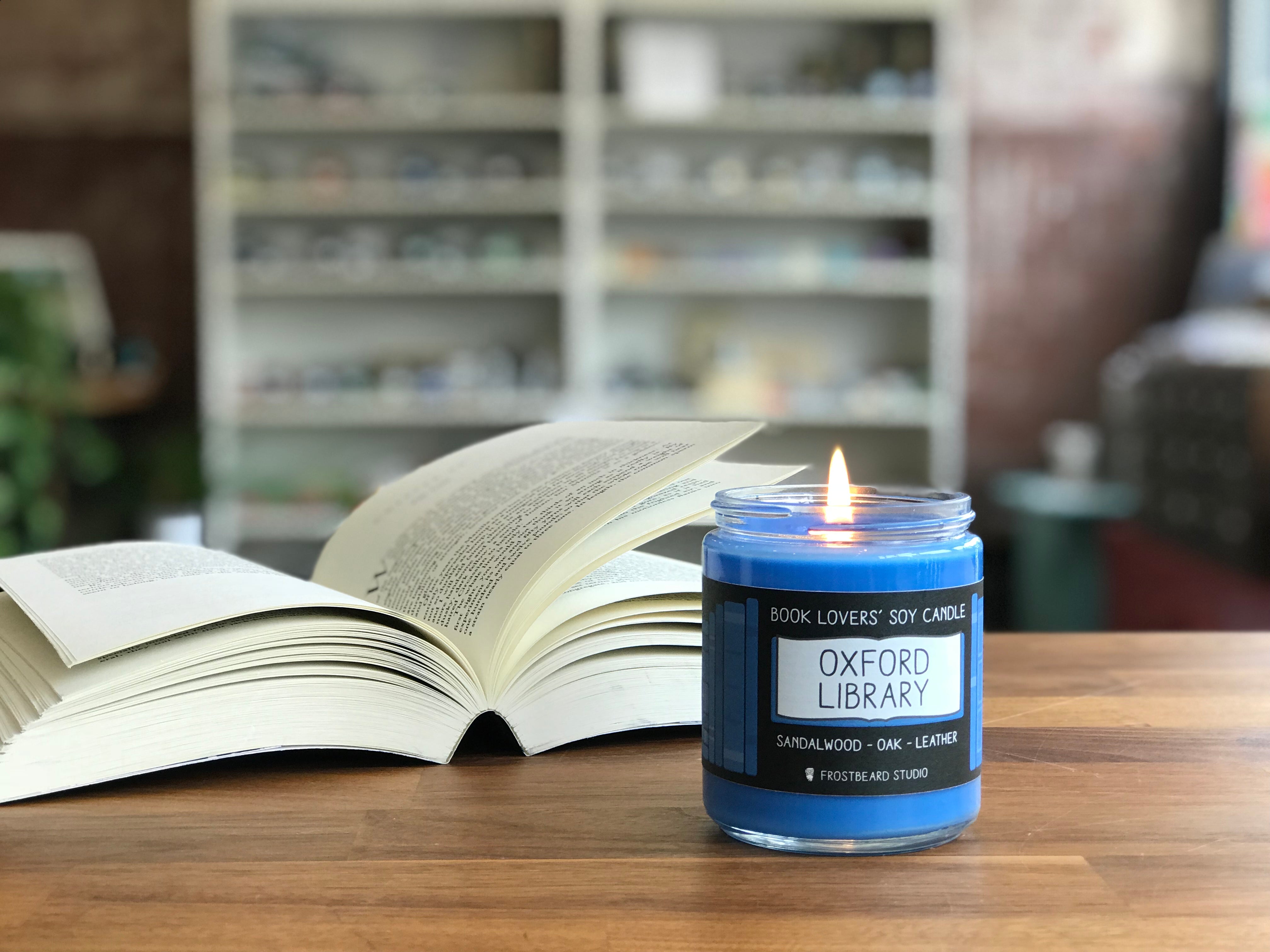 A lit blue wax Frostbeard candle on top of a wooden table next to an open book