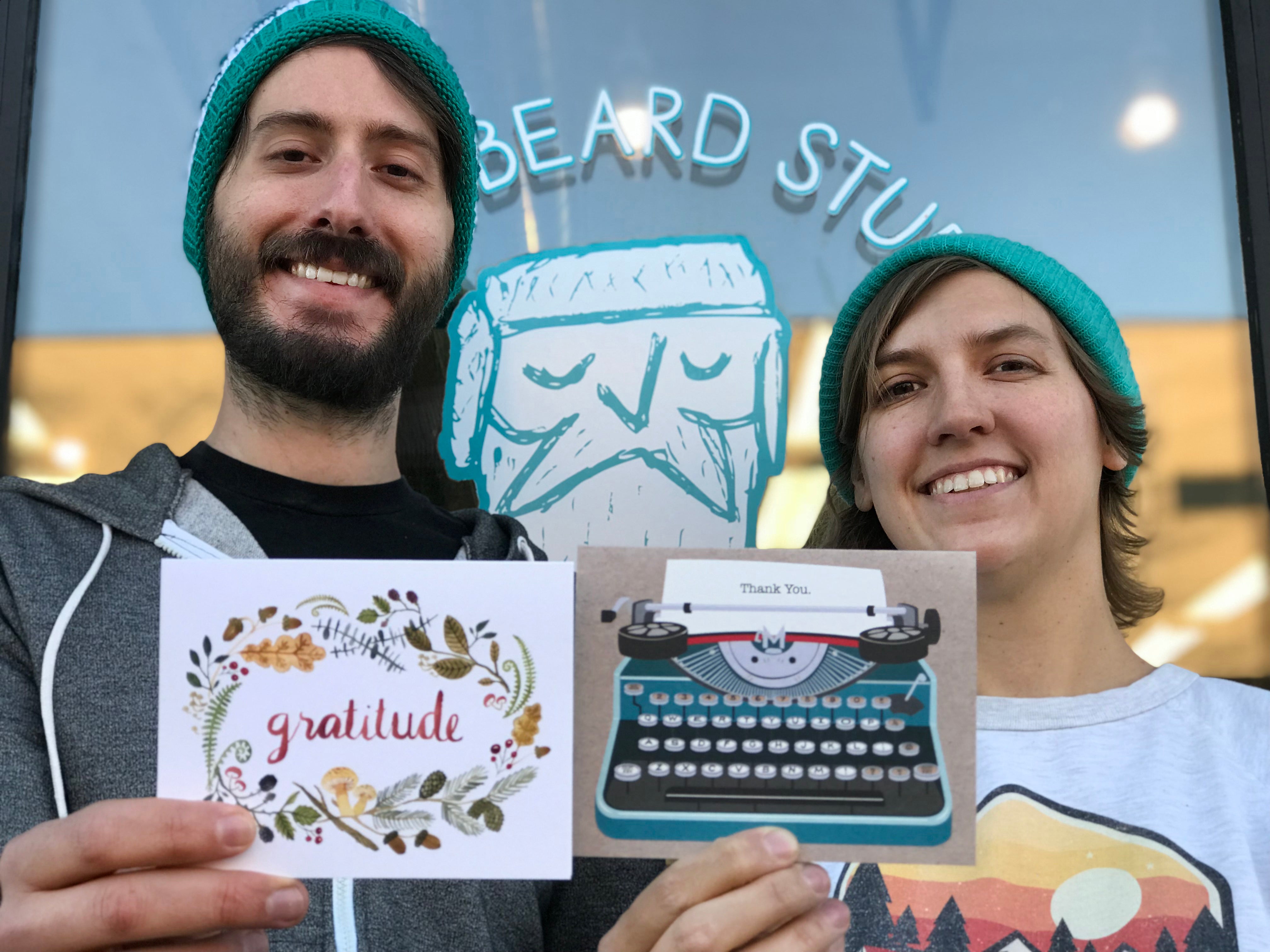 Tom and Roxie founders of Frostbeard standing outside their studio holding up greeting cards