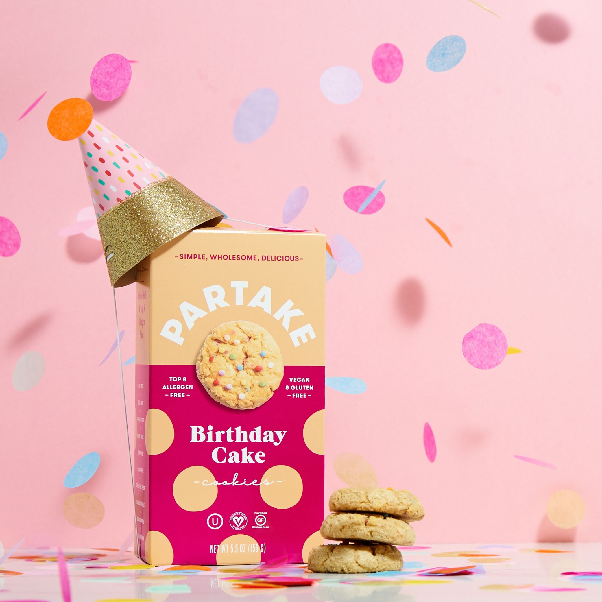 A box of Birthday Cake cookies topped with a party hat with confetti in the photo along with three cookies outside of the box. 