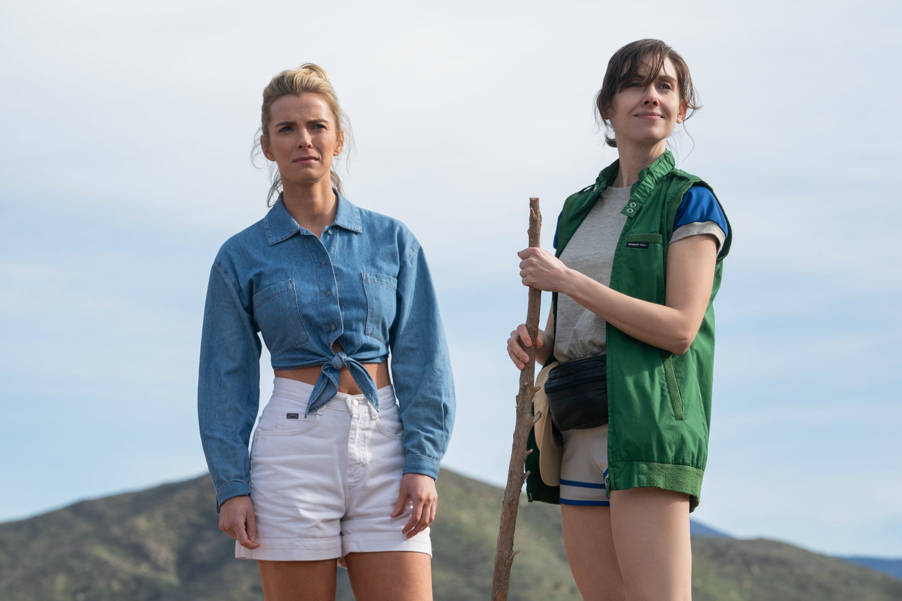 Ruth and Debbie stand on top of a hill during a hike outside of Las Vegas. Debbie is holding a hiking stick, and they are both looking into the distance. 