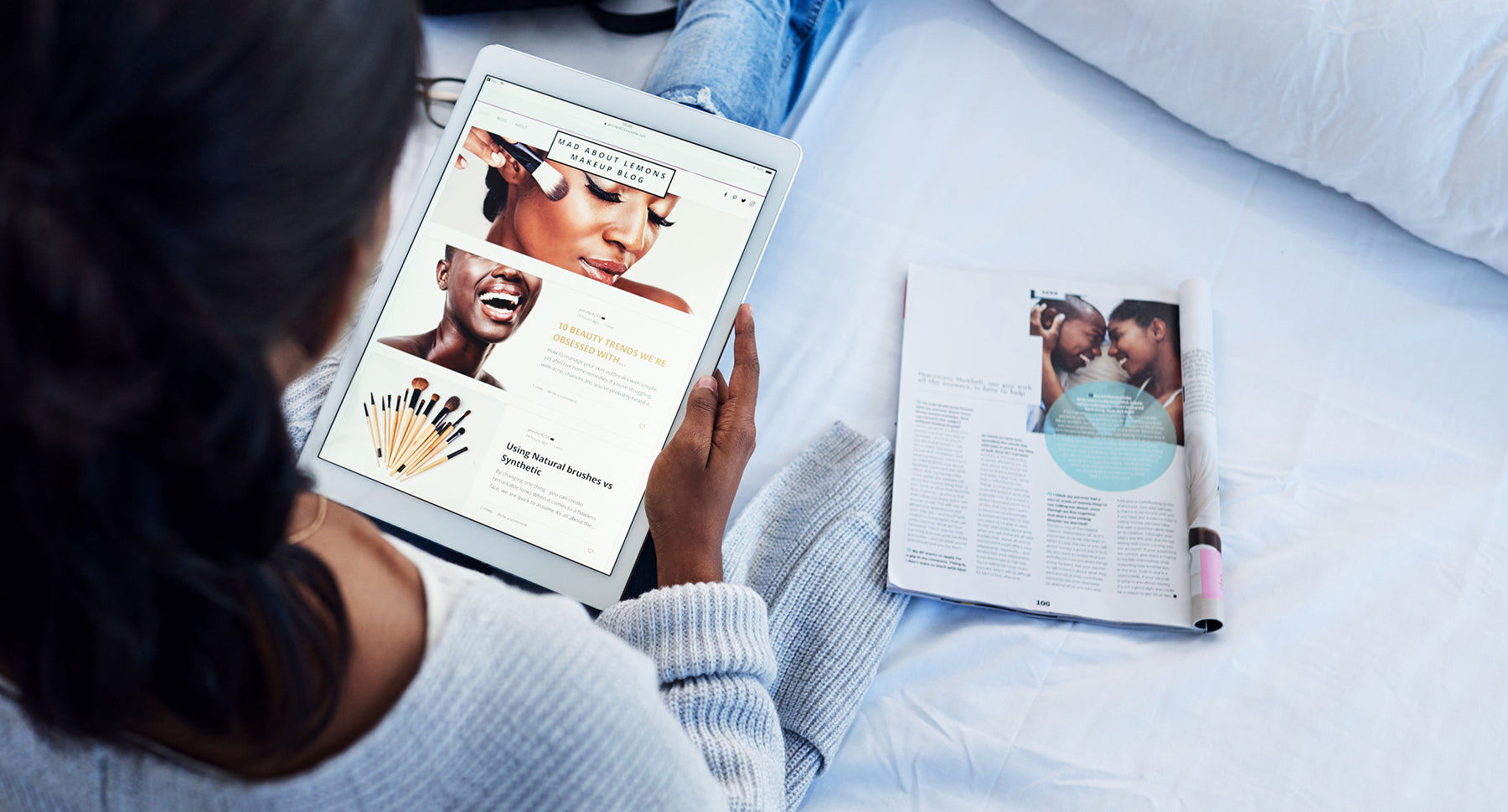 over the shoulder photograph of a young black woman sitting on her bed looking at a makeup blog on ipad