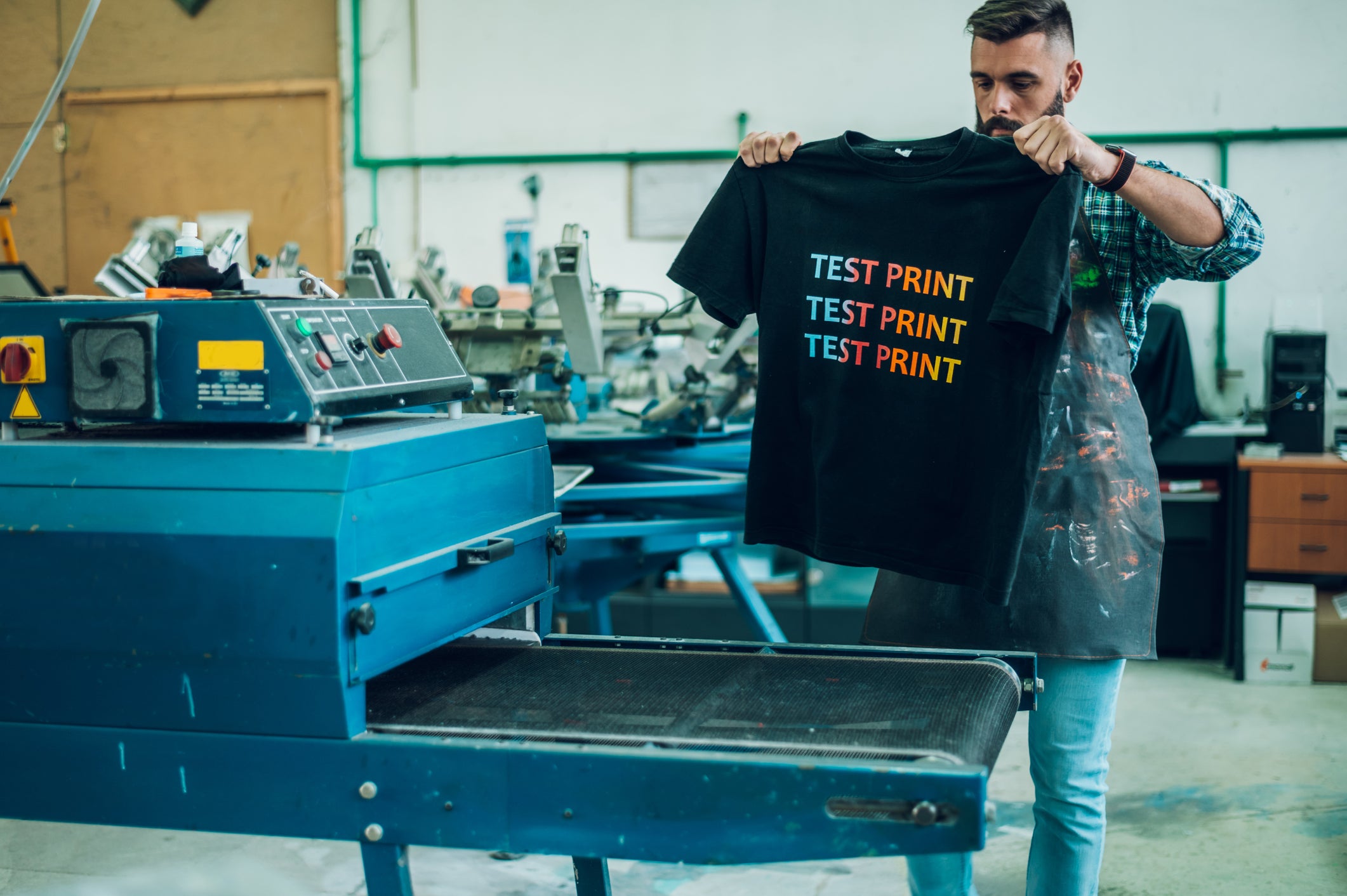 一个男人在车间印刷机前展开一件T恤
