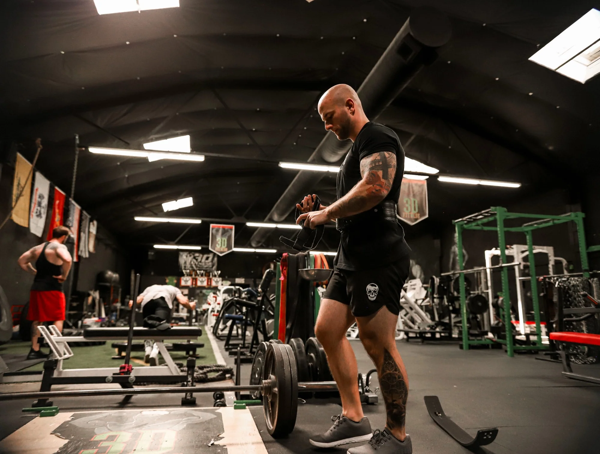 Roc Pilon of Gymreapers in a gym setting wearing clothing by Gymreapers while he puts on lifting gloves. 