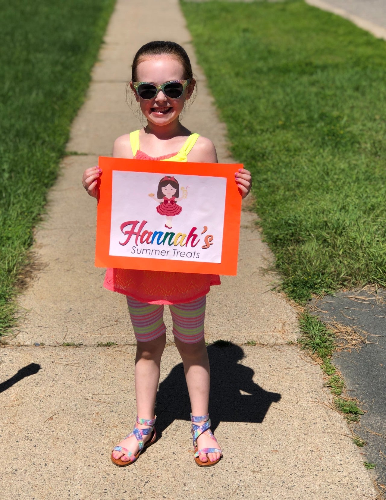 Hannah stands on the sidewalk holding a promotional sign for Hannah's Treats.