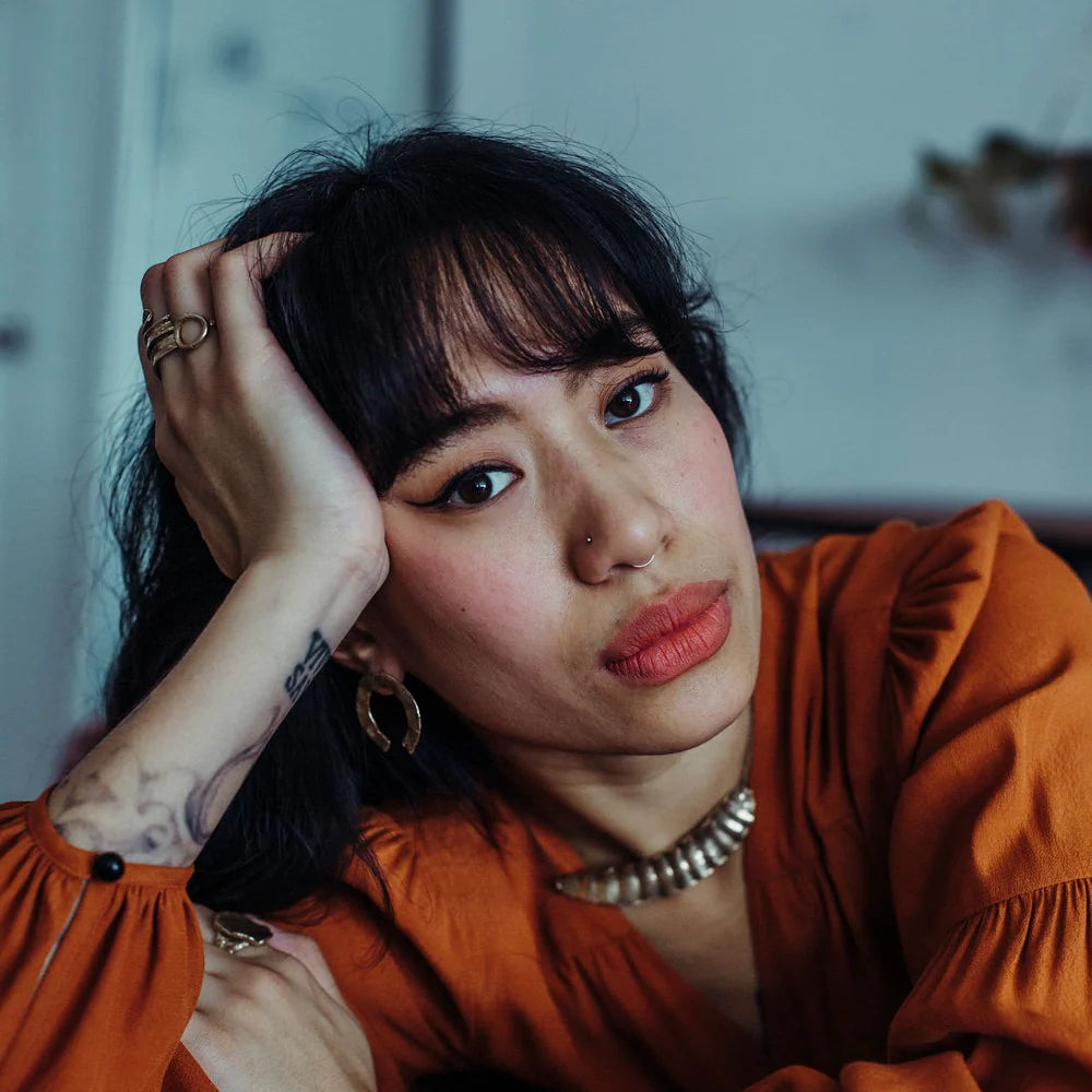 A woman leans her head  on her hand while modelling jewelry