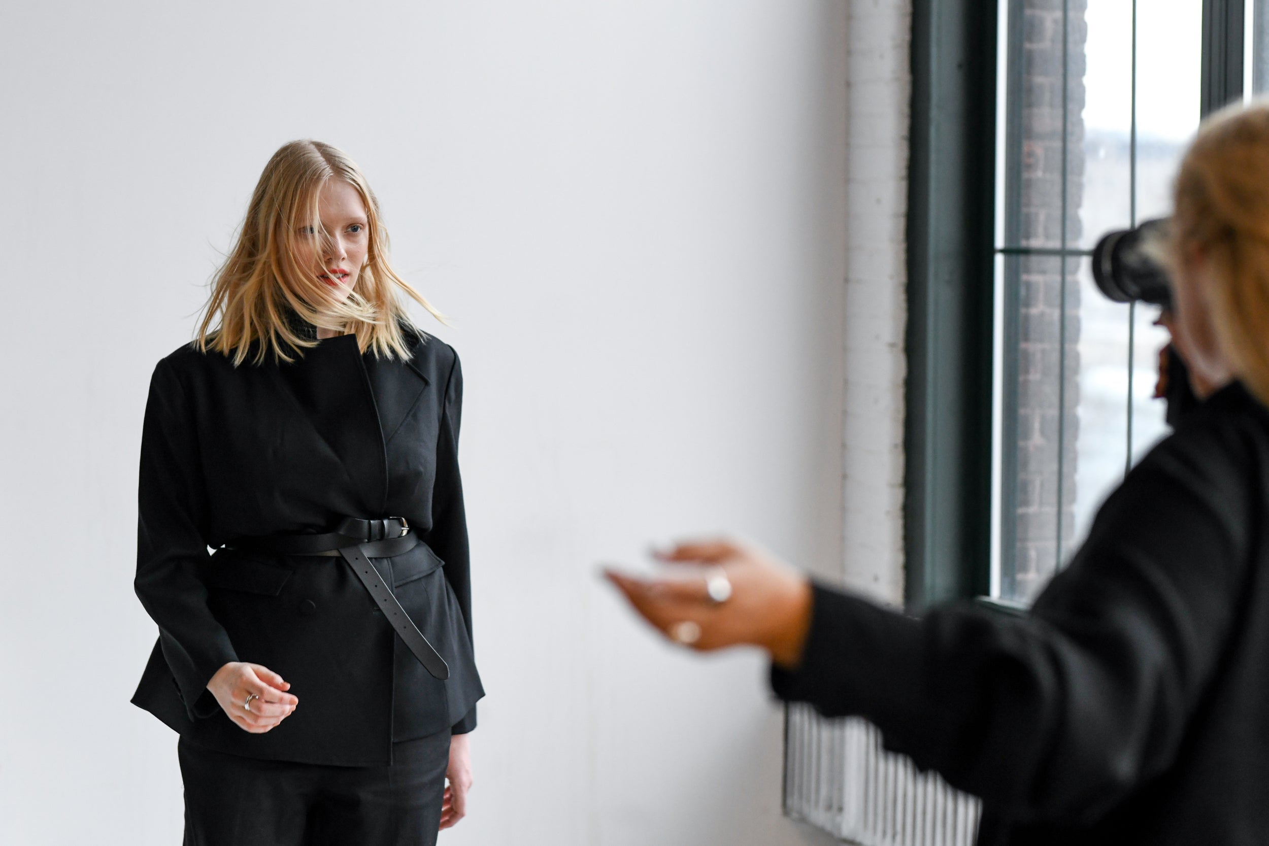 Model met blond haar poseert in een zwarte jas voor een fotoshoot