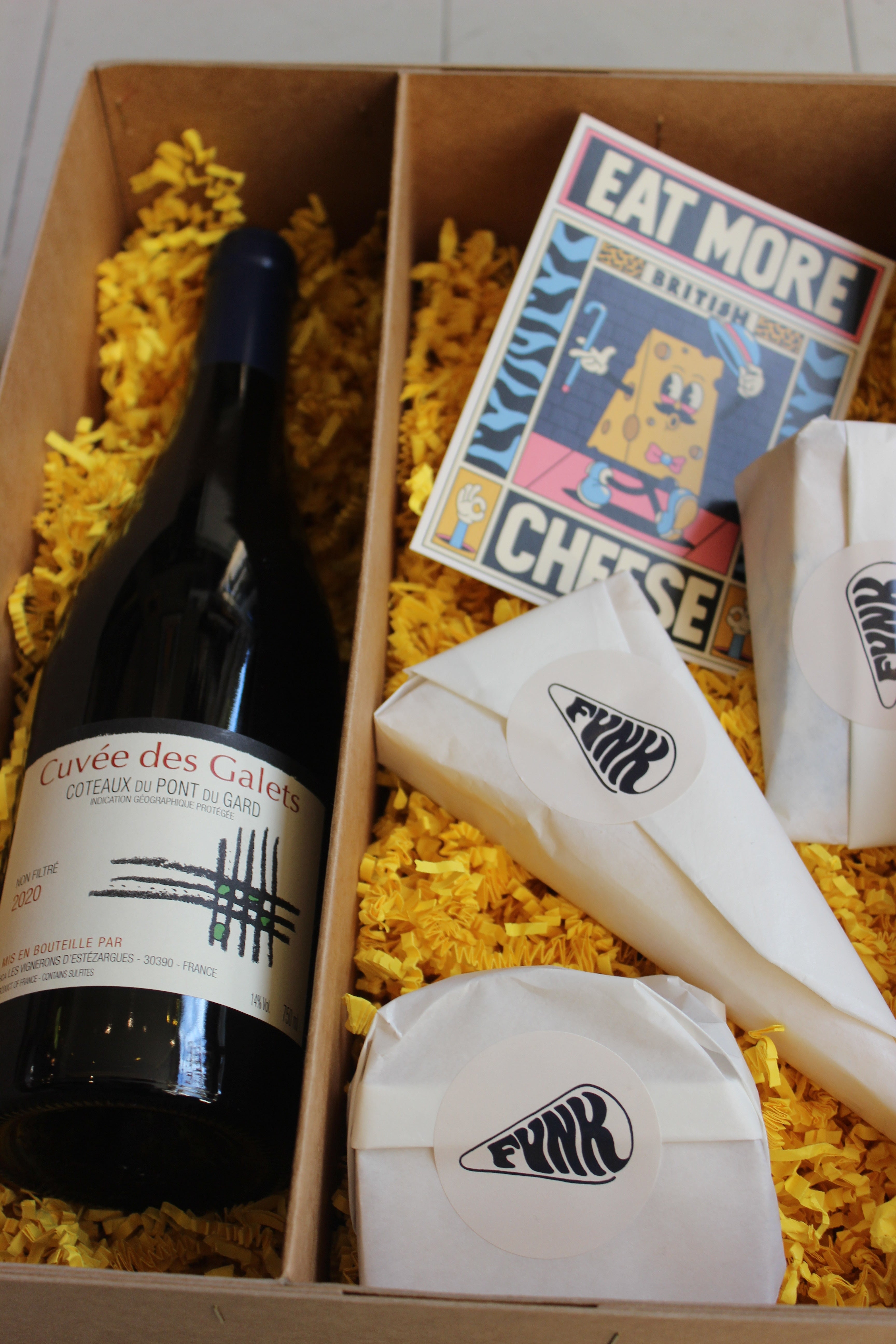 A box by Funk filled with a bottle of wine, cheeses, and a poster. 