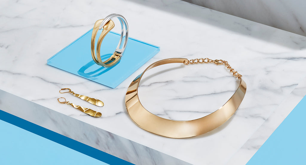 A gold bracelet, necklace, and earrings sitting on a white marble slab.