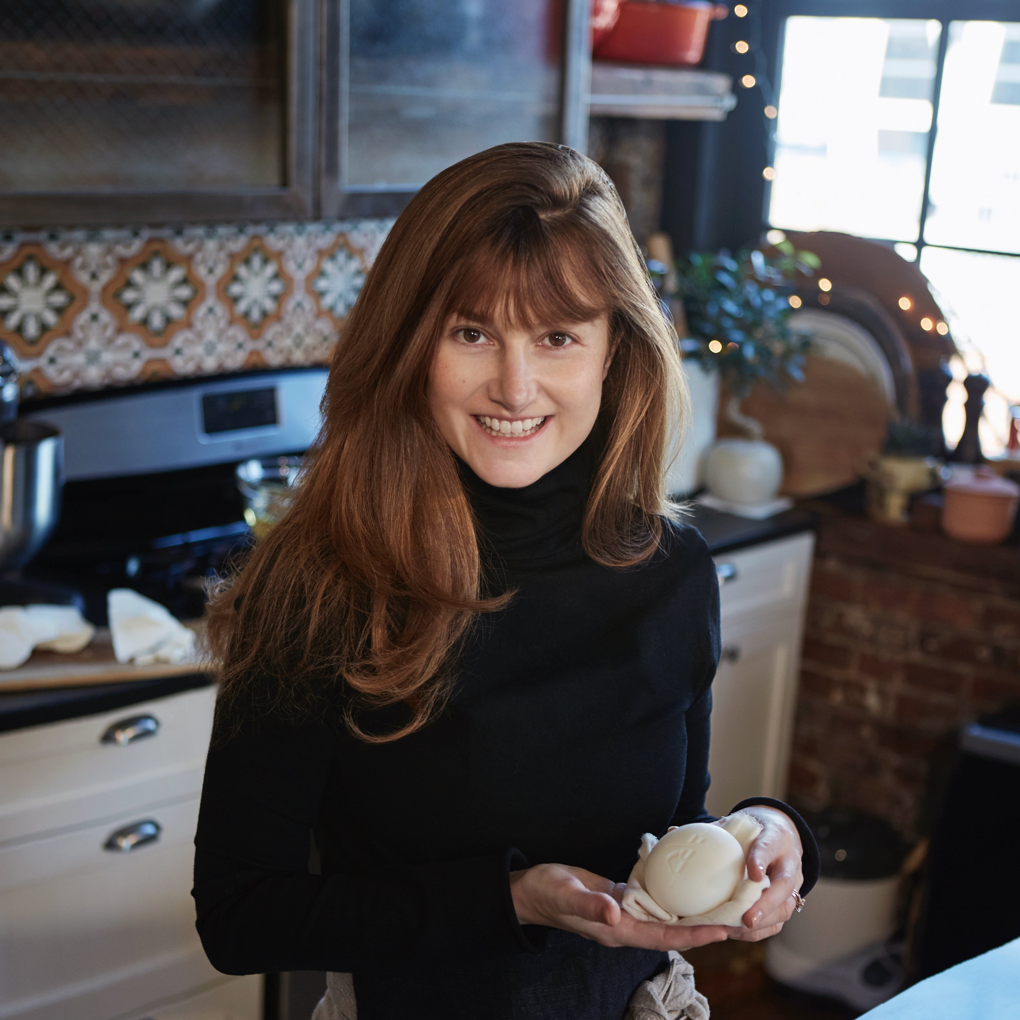  Kate McLeod dressed in a black turtleneck holding a Body Stone within her kitchen. 