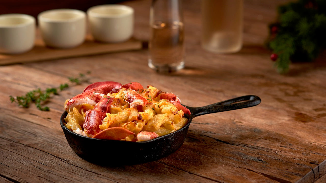 A cast-iron pan filled with lobster mac and cheese against a wooden kitchen counter. 