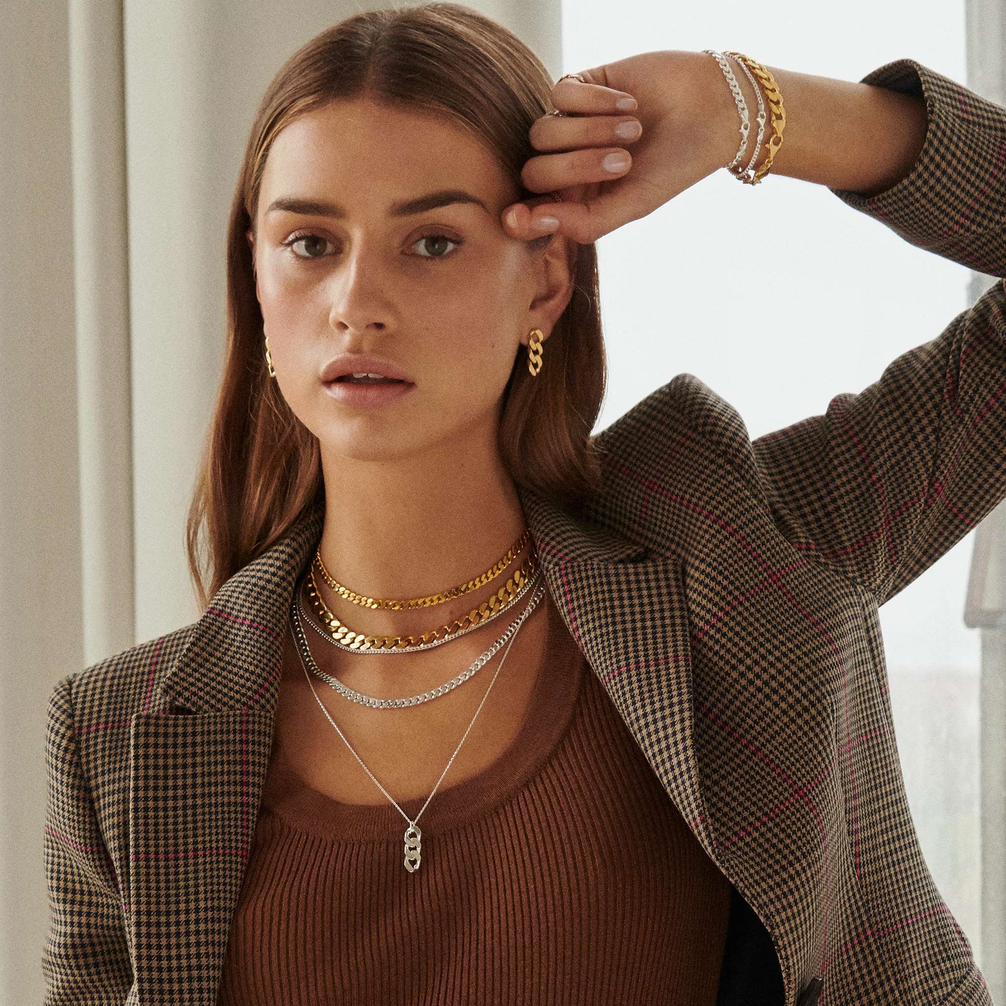 A model in a brown patterned jacket wears multiple pieces of earrings, necklaces, and bracelets from Camille Brinch. 