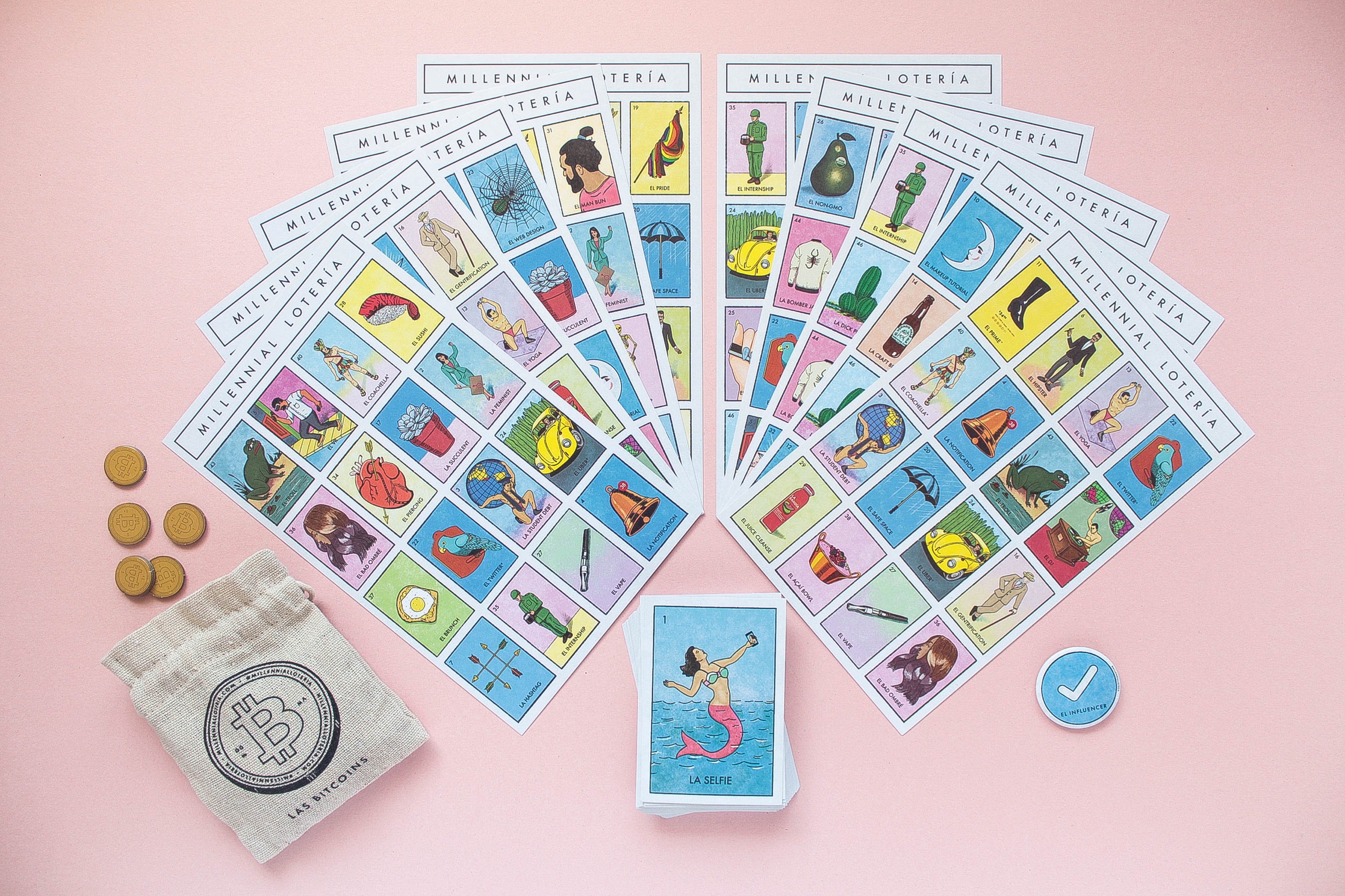 A set of Millennial Loteria cards and coins fanned out on a pink background