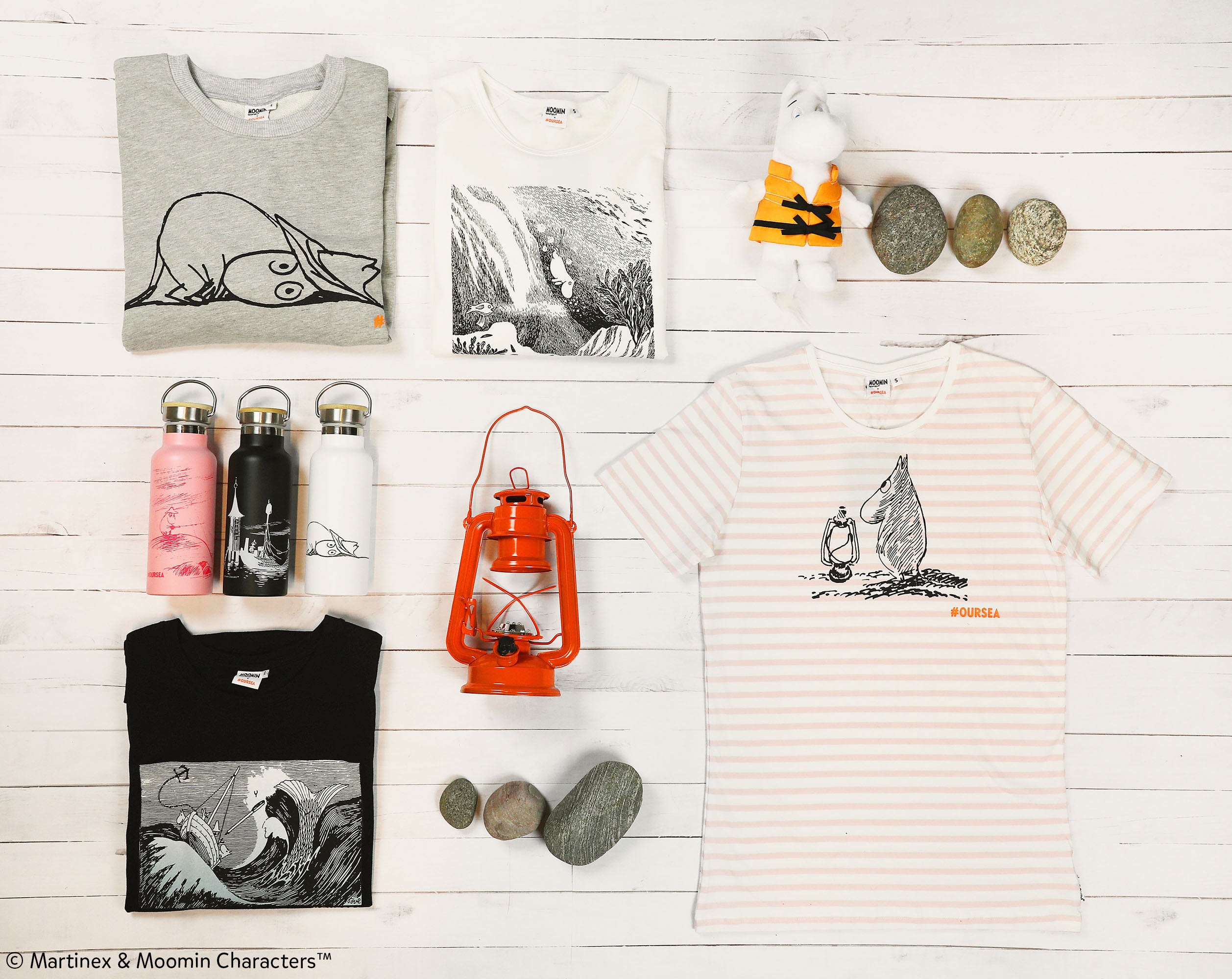 A selection of Moomin merchandise in a flat lay, complete with t-shirts, water bottles, and stuffed animals. 