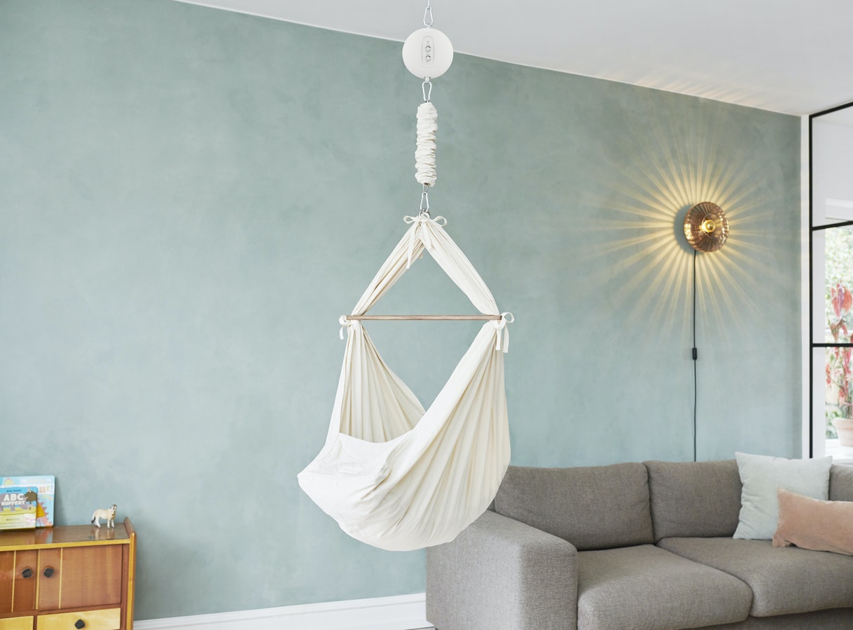 A fabric baby hammock by Moon Boon is hanging from the ceiling in a living room setting. 