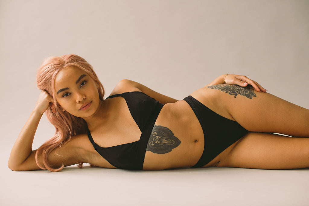 A model lying on her side with her head perched on her hand wearing a black set by Pantee