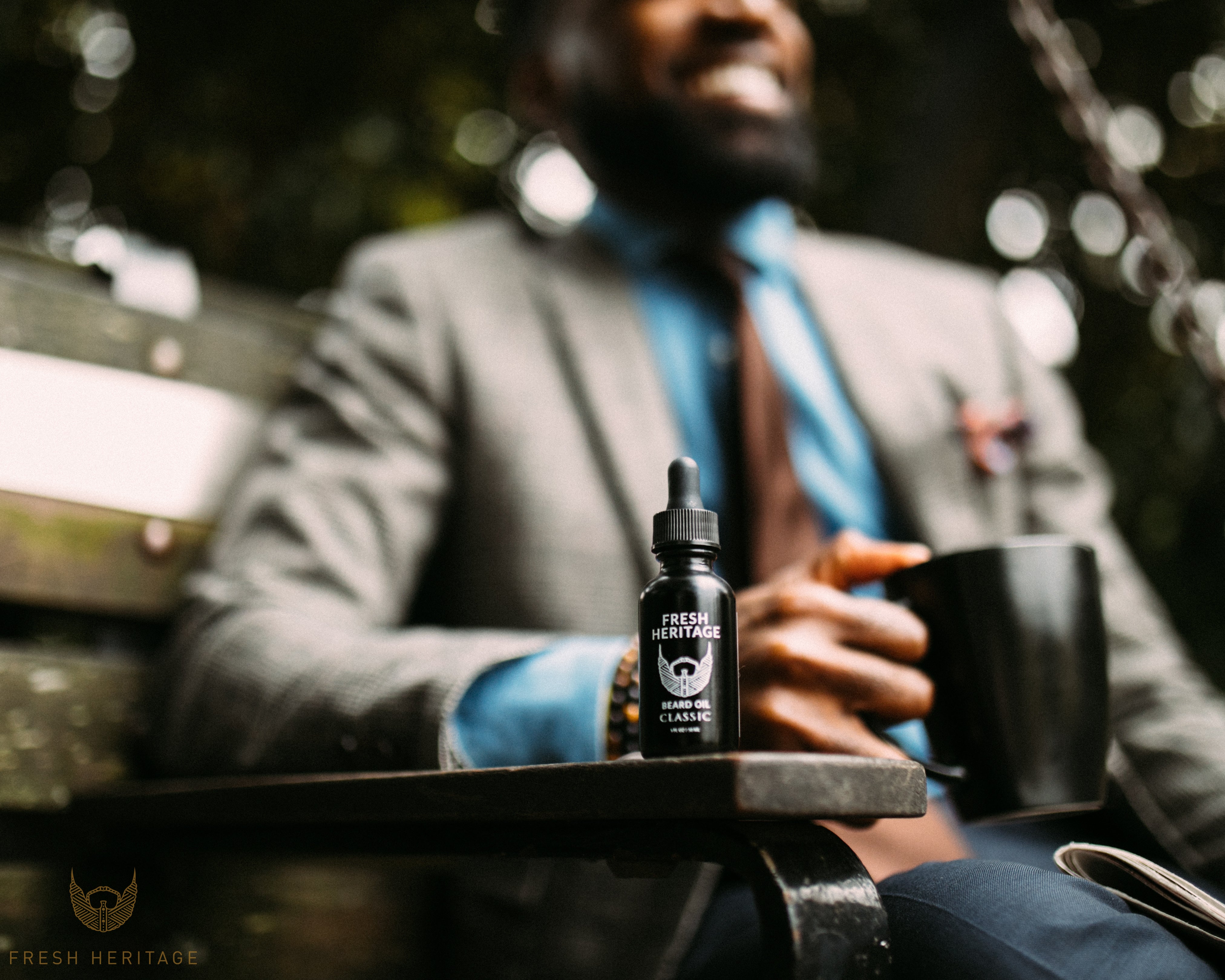 A model in a suit with a coffee backdrops a bottle of beard oil by Fresh Heritage. 