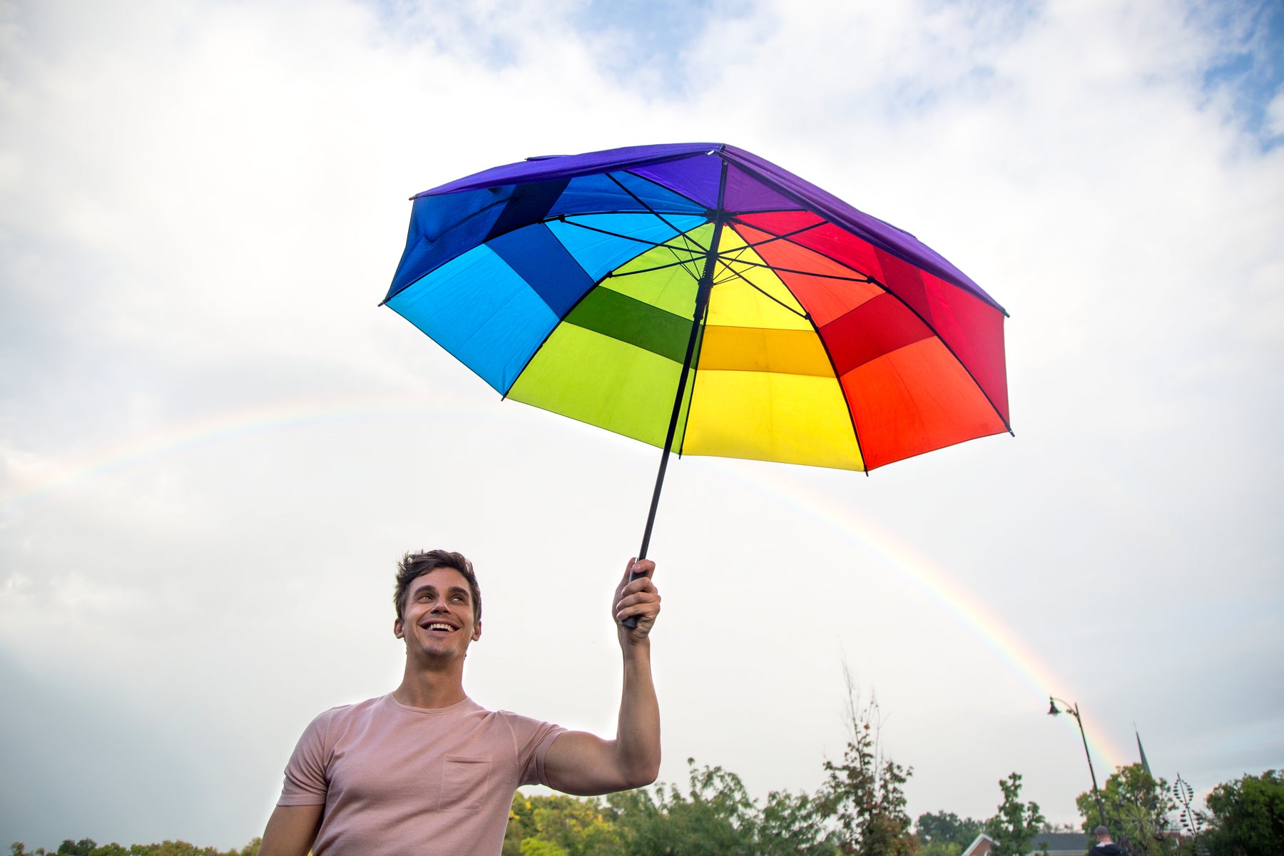 Antoni holds a rainbow umbrella against a sky with a rainbow in an episode of Queer Eye.