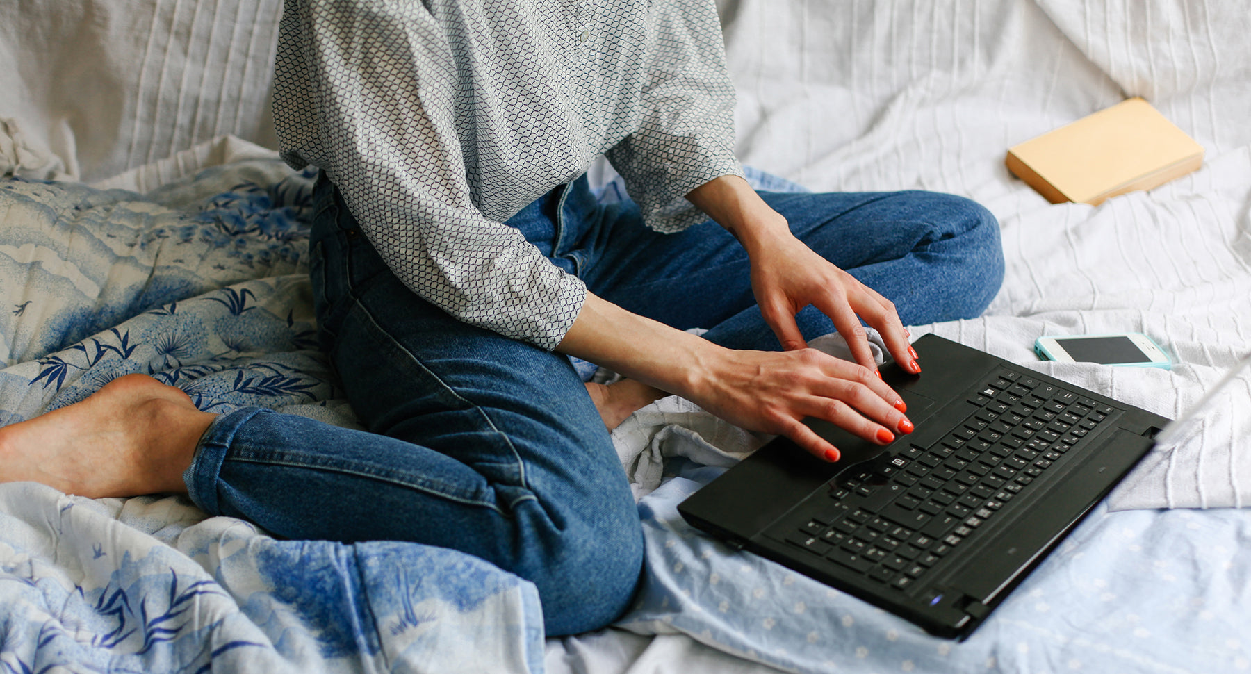 female subject sitting on her bed in blue jeans typing on her laptop and registering her domain name