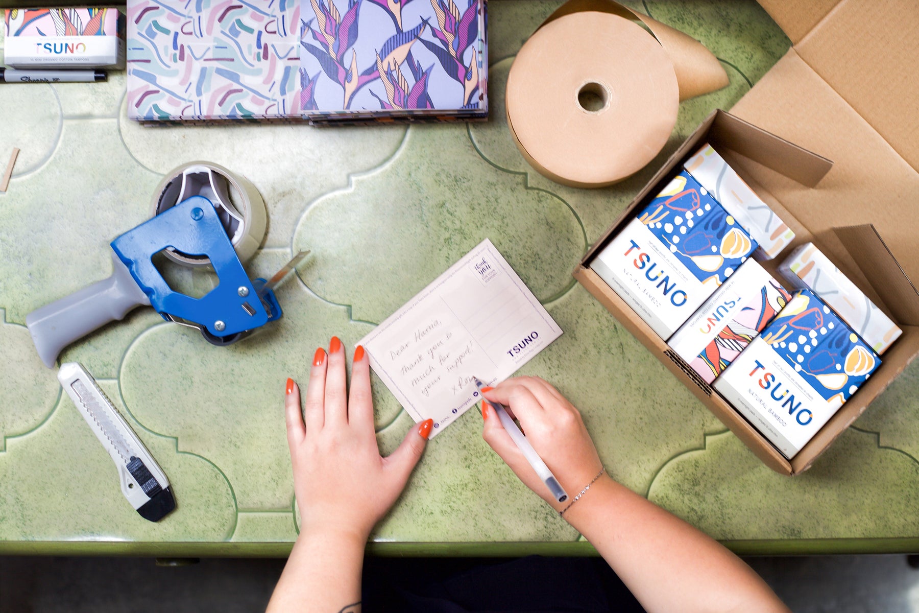 Close up of hands packaging Tsuno feminine hygiene products, and writing a thank you card.