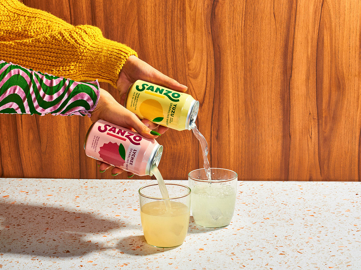 Two hands pouring cans of Sanzo sparkling water into cups