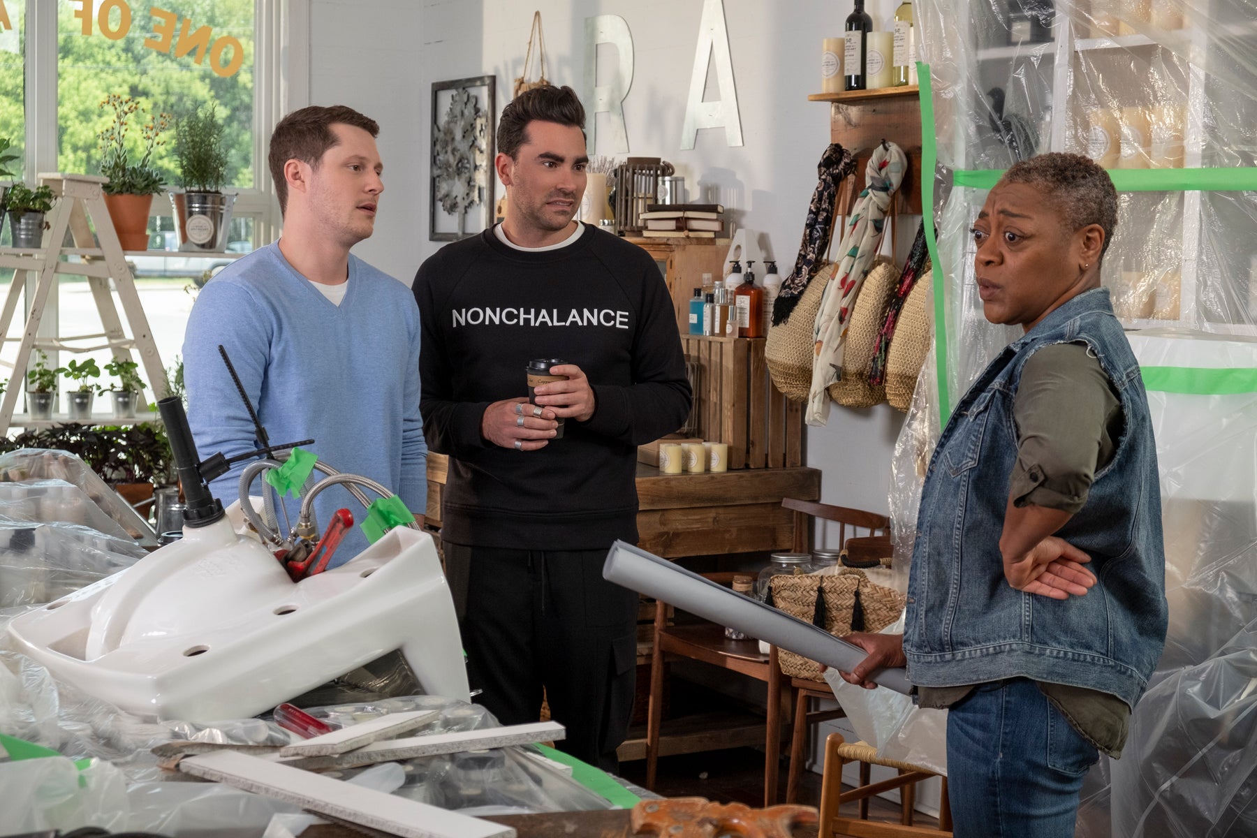 David Rose, Patrick, and Ronnie stand in the middle of a store currently undergoing renovations. A sink sits atop construction rubble in the foreground.