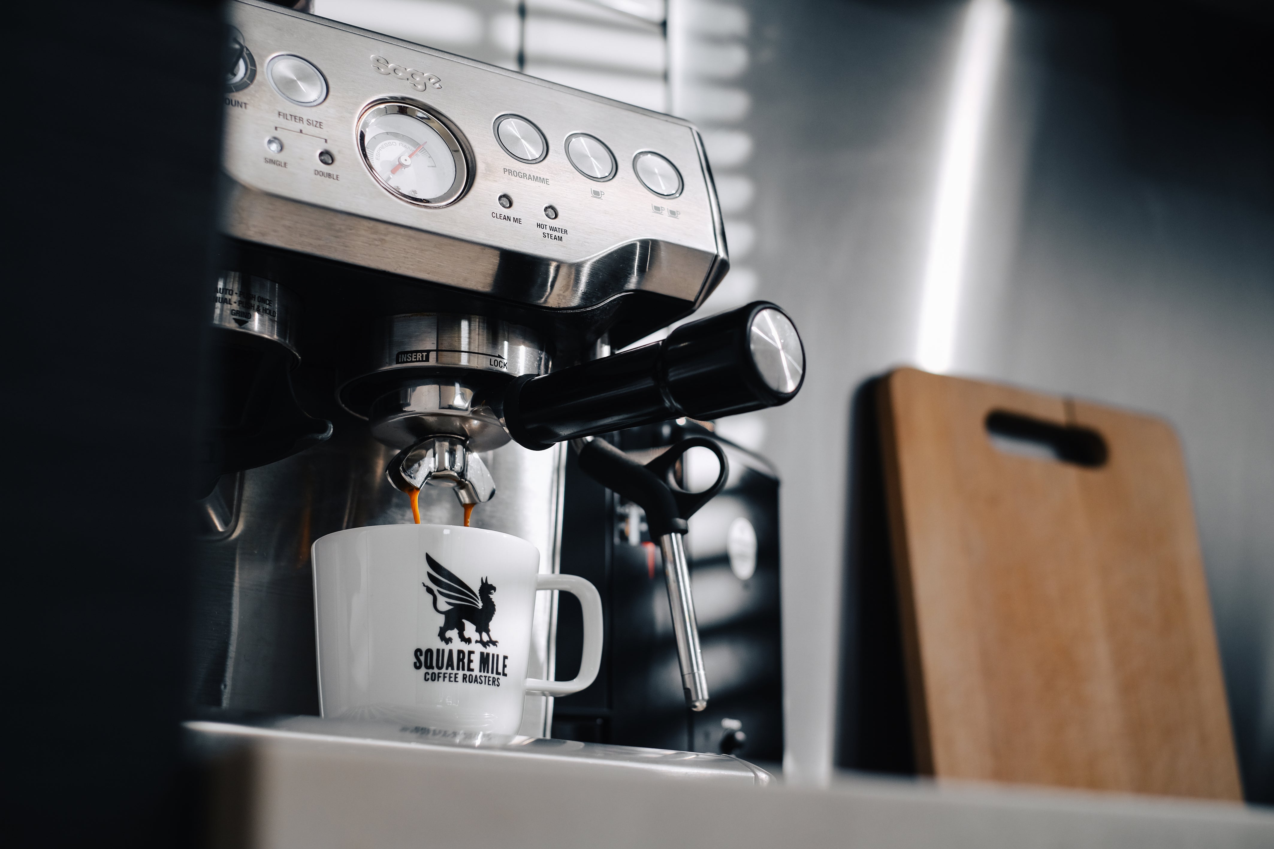 A white Square Mile Coffee Roasters cup backdropped by an espresso machine. 