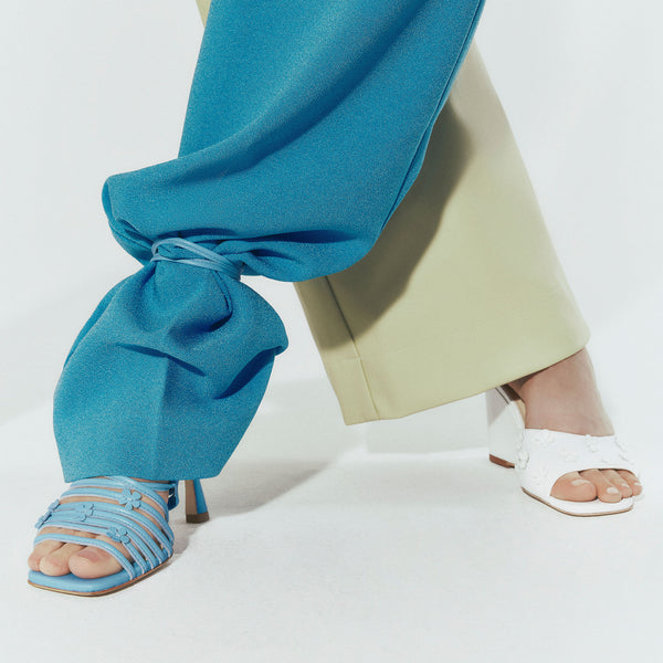 One foot wearing a blue Maguire sandal and one foot wearing a white Maguire heel