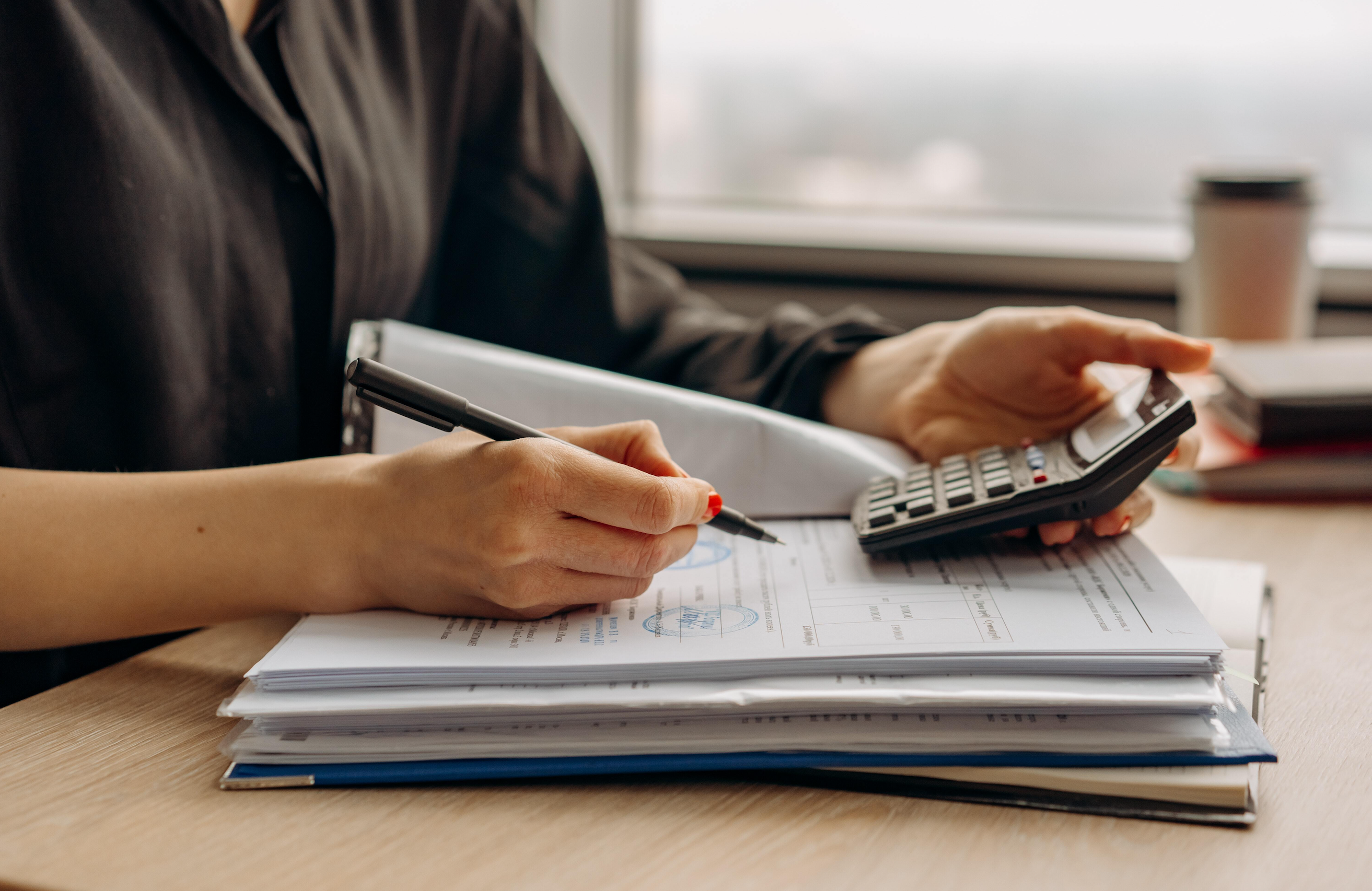 a mids hot of a woman's handholding a calculator with one hand and writing notes with the other hand