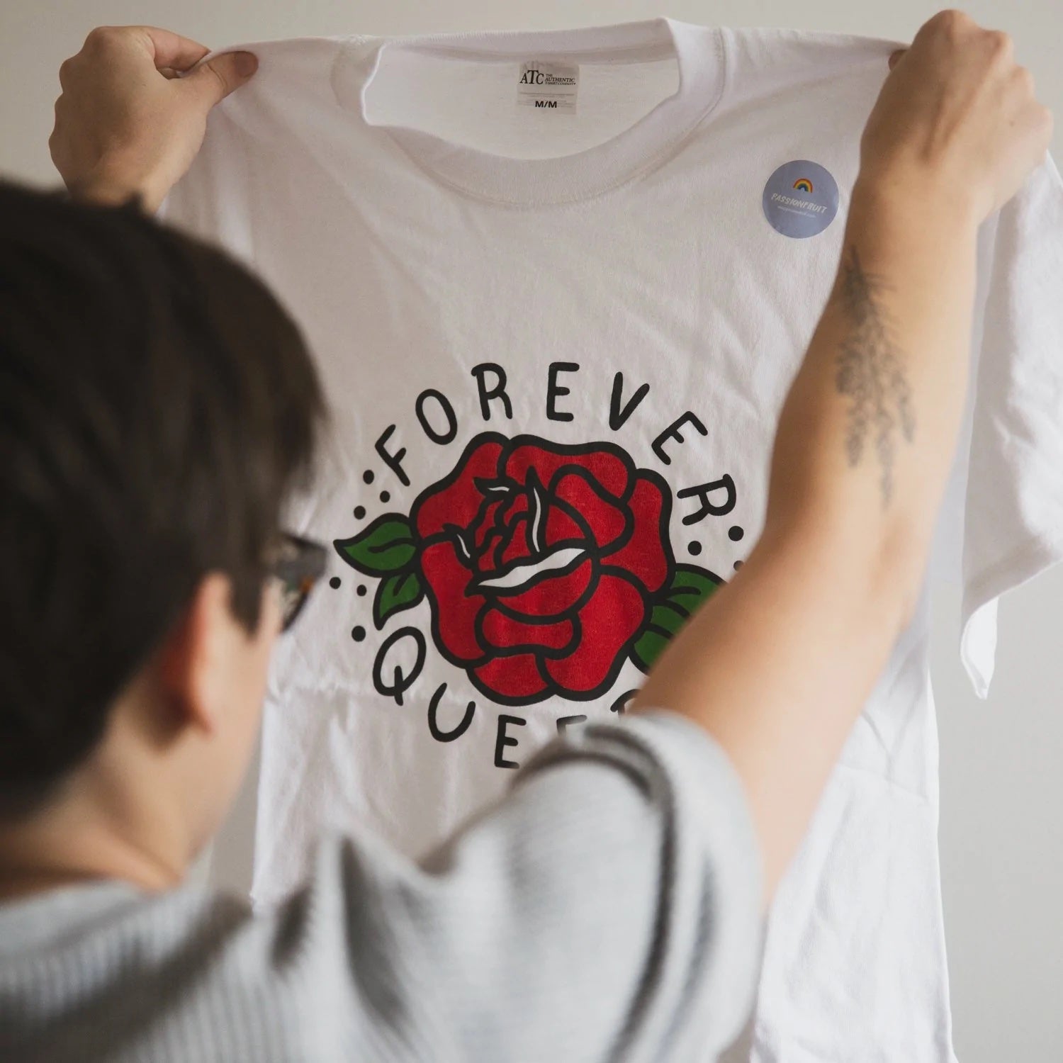 A person holds up a graphic t-shirt that reads "forever queer"