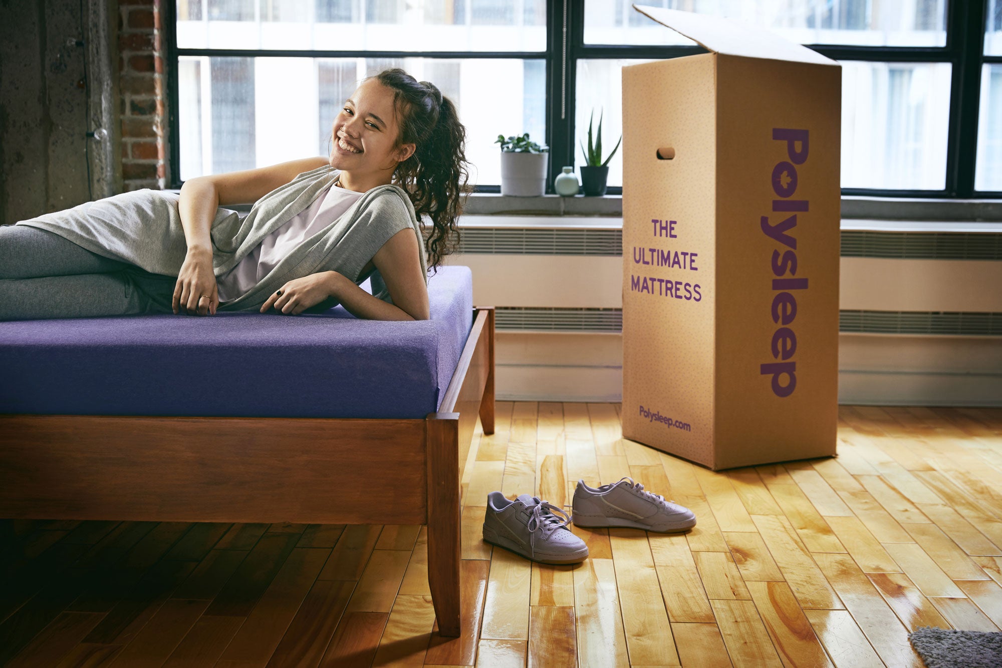 Shopify Masters: BFCM roundup, Polysleep founder Jeremiah Curves lying on a bed with purple sheets and an open Polysleep box beside it, with windows in the background