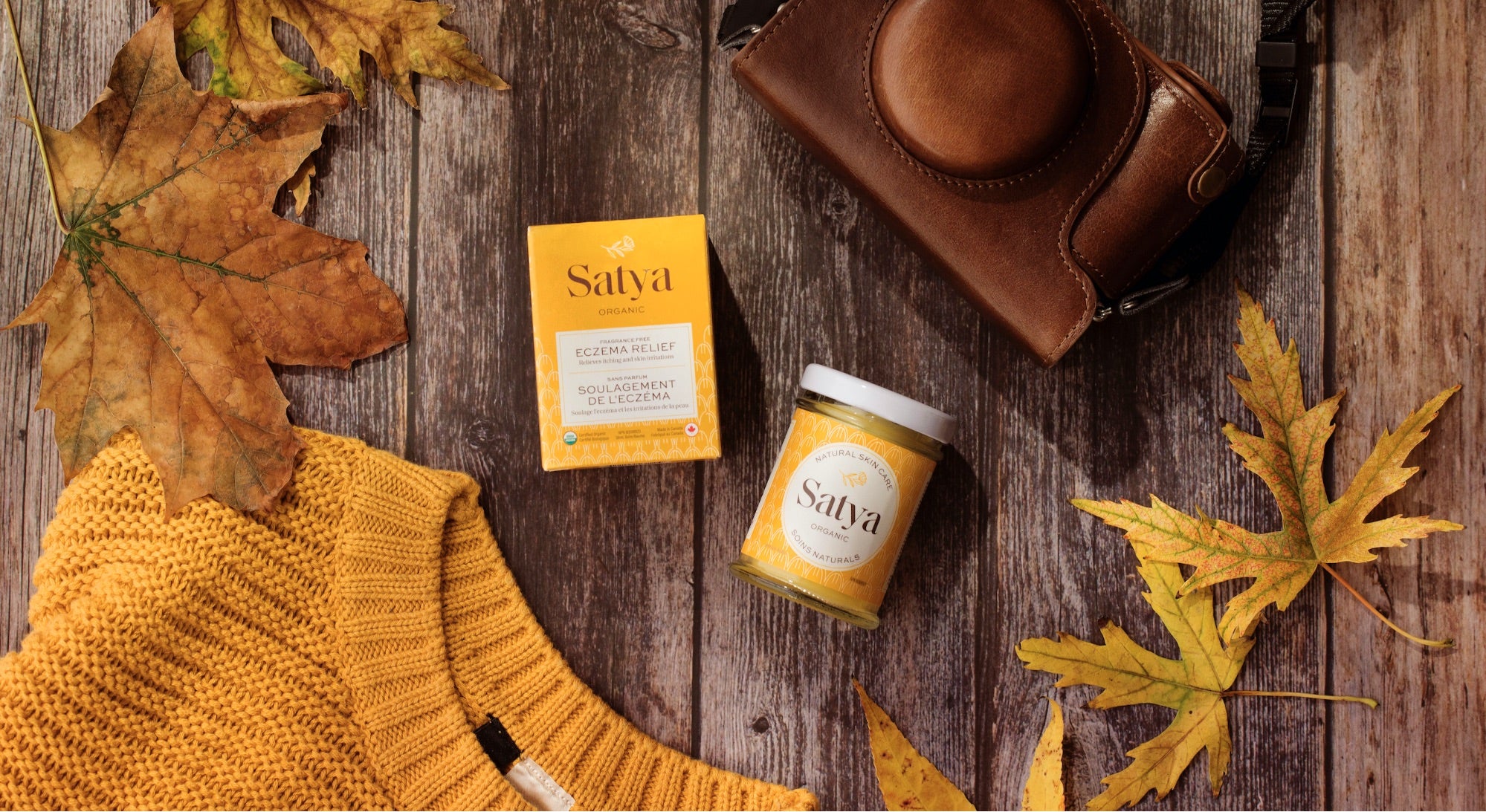 Shopify Masters: a flatlay of Satya products against a rustic, automnal backdrop featuring leaves, a camera and a yellow sweater