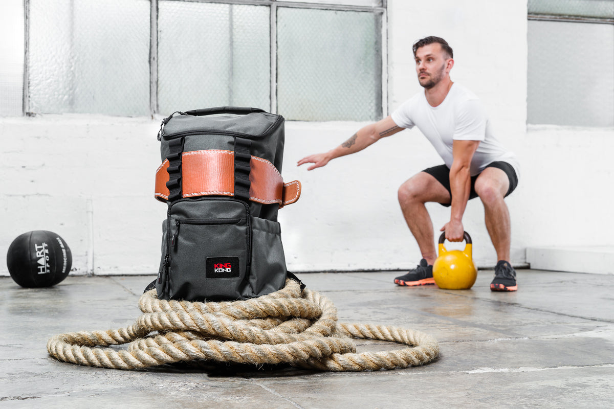 A male model with a kettlebell backdropping a backpack made by King Kong Apparel. 