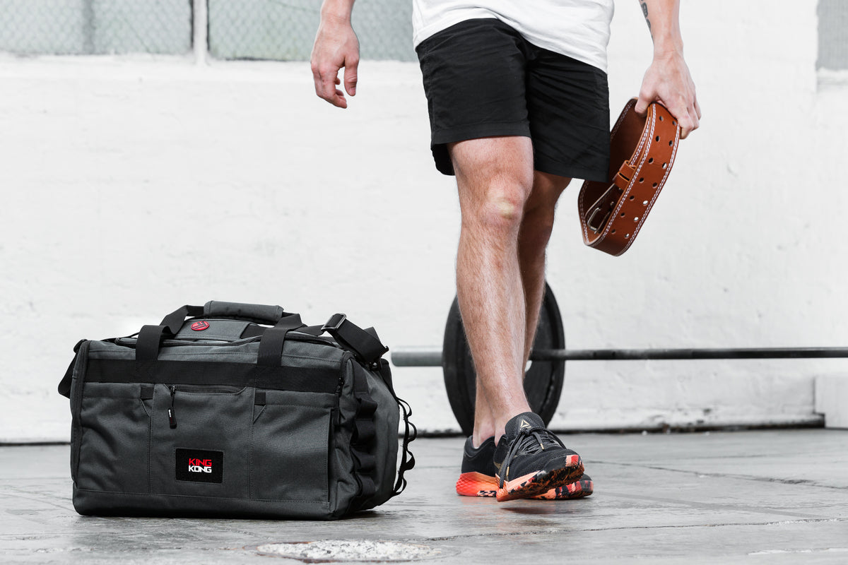  A male model in shorts and running shoes standing next to a duffle bag designed by King Kong Apparel specifically for CrossFit. 