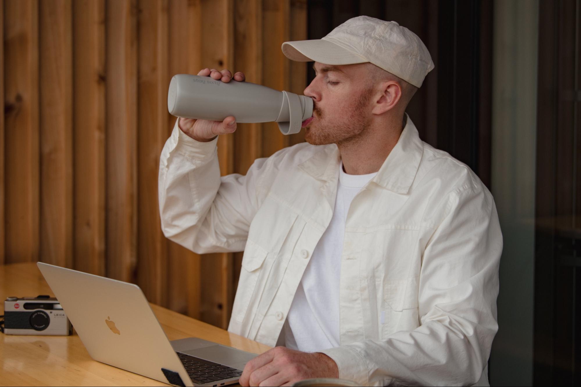 A male model drinks from a stone colored water bottle by Stay Sixty. 